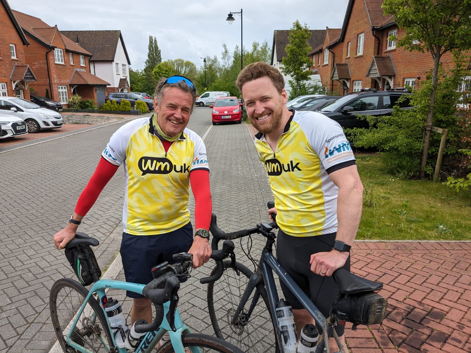 Bob standing beside his son, both wearing cycling gear and holding two bikes upright 