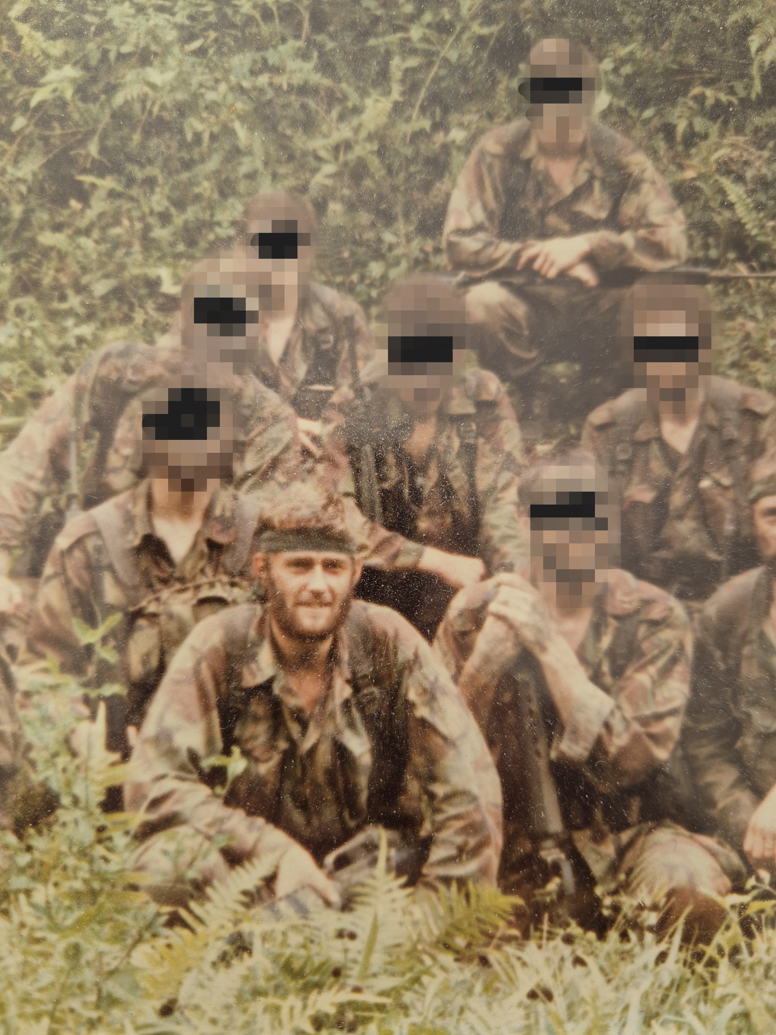 A picture of Bob crouched in the jungle in front of a group of other soldiers in training, whose faces have been blurred 