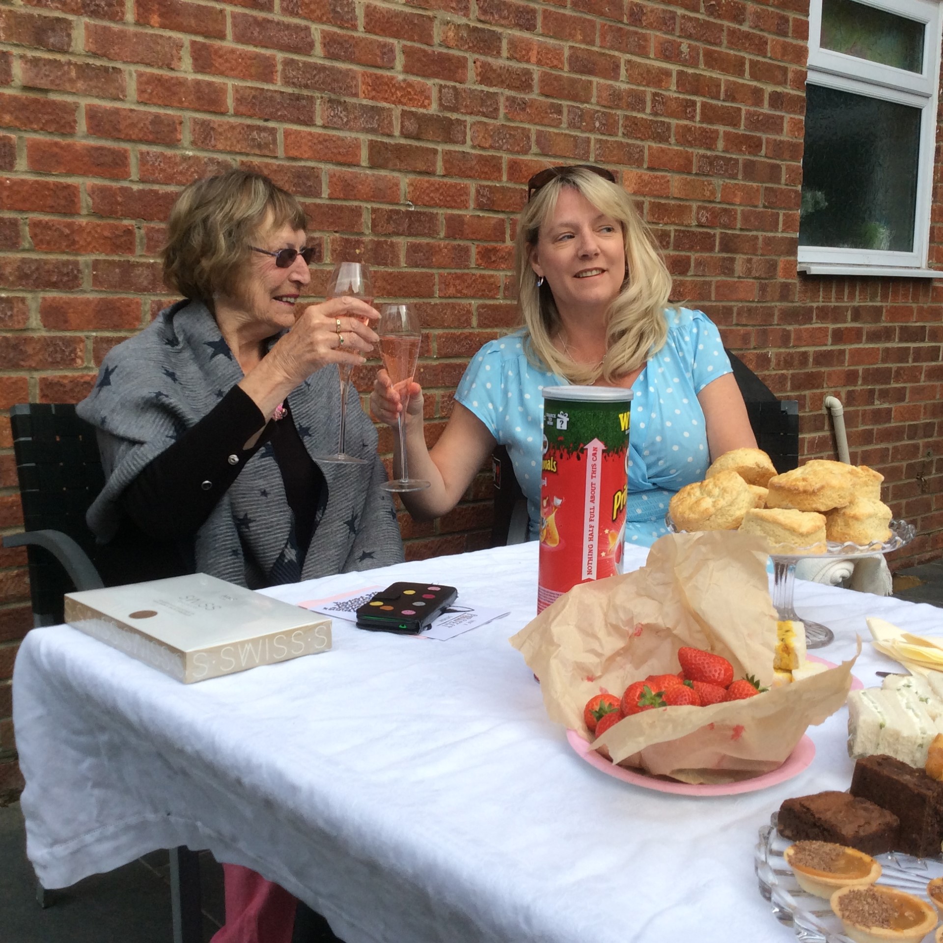 Helen and her mother sitting side by side at a table and clinking their glasses together 