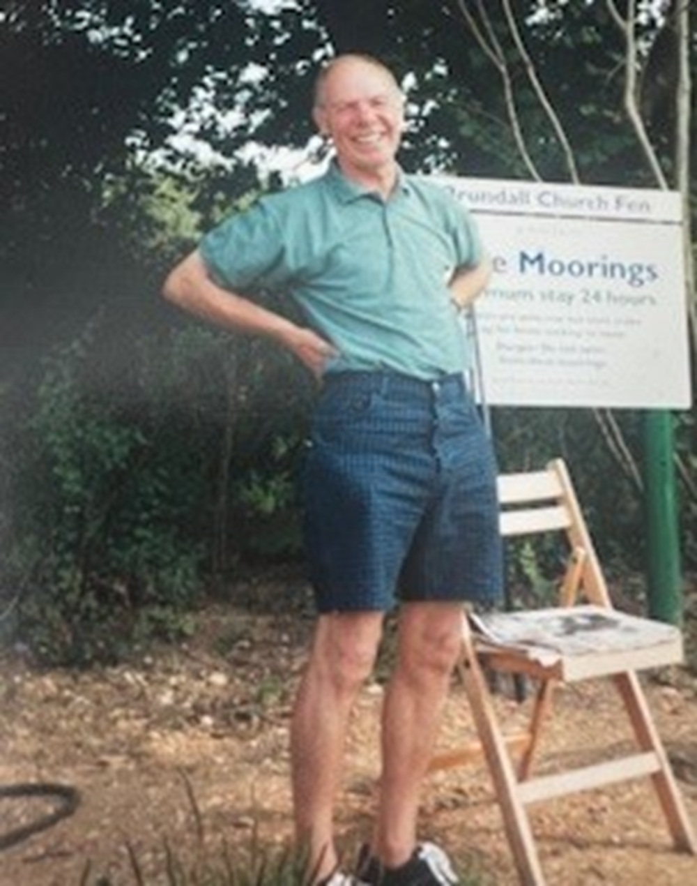 Helen's father, Keith, wearing a blue top and shorts and smiling with his hands on his hips