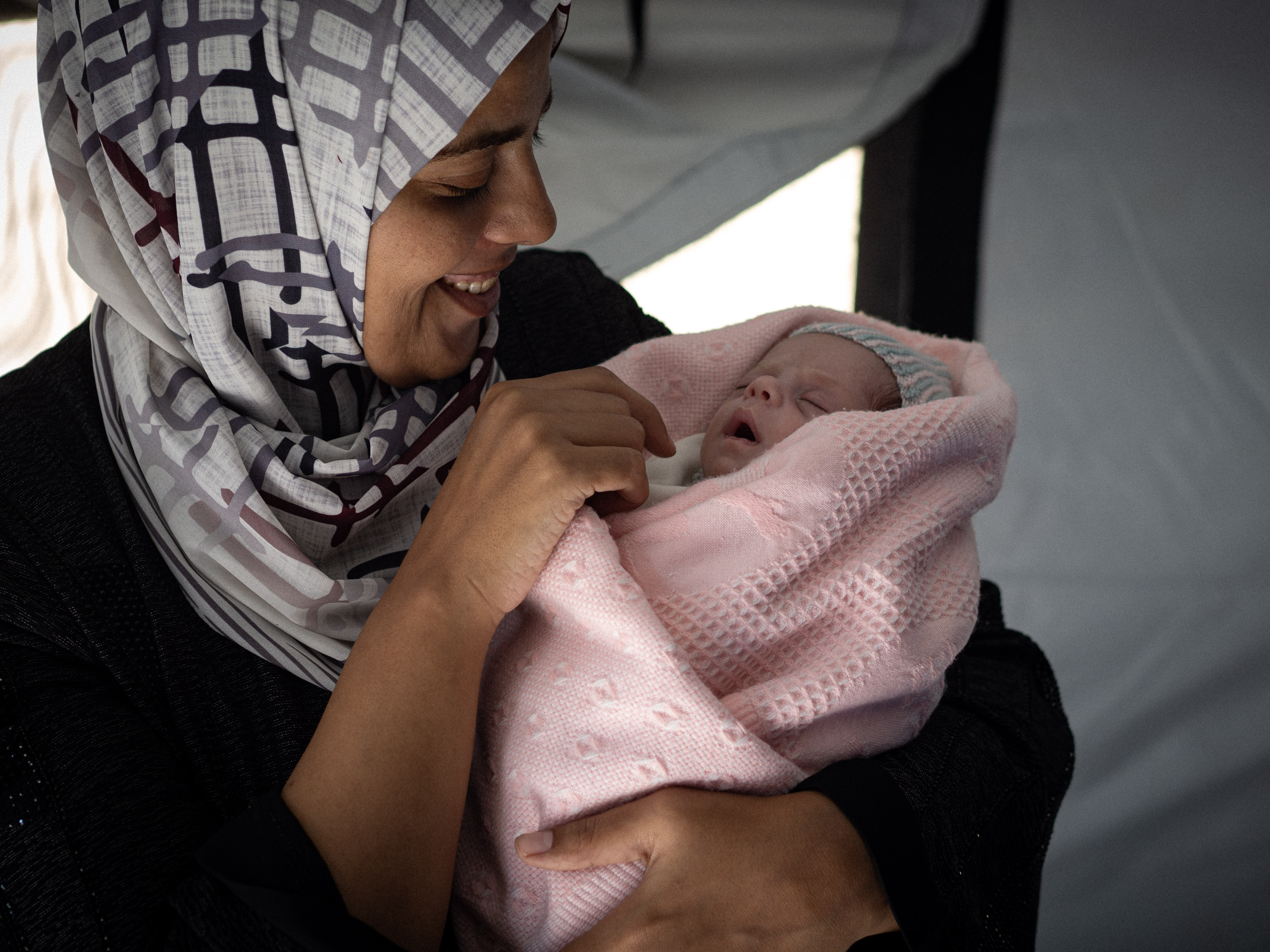 A woman smiles while holding a newborn wrapped in a pink blanket