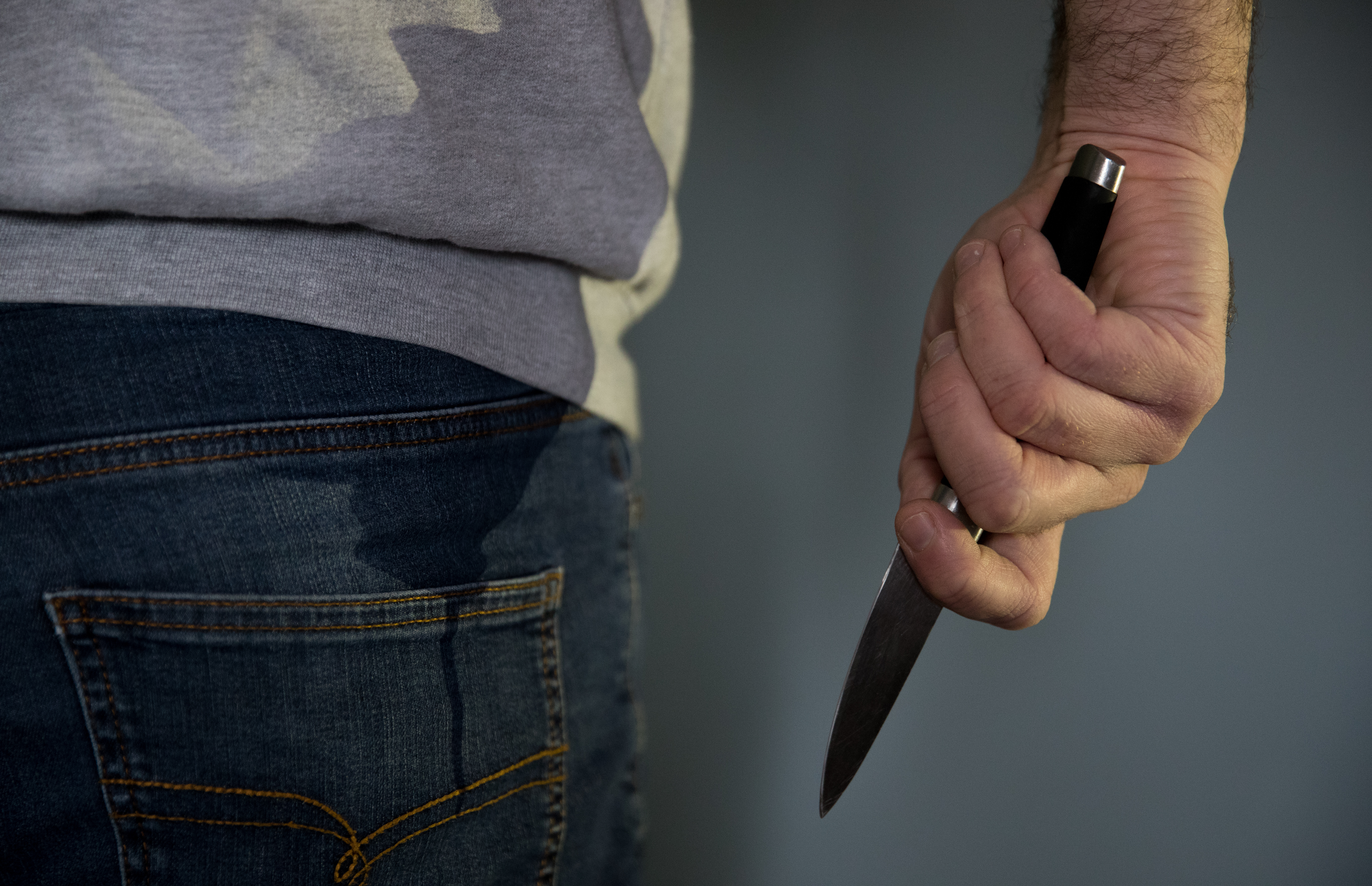 A person holding a knife seen from behind, waist down
