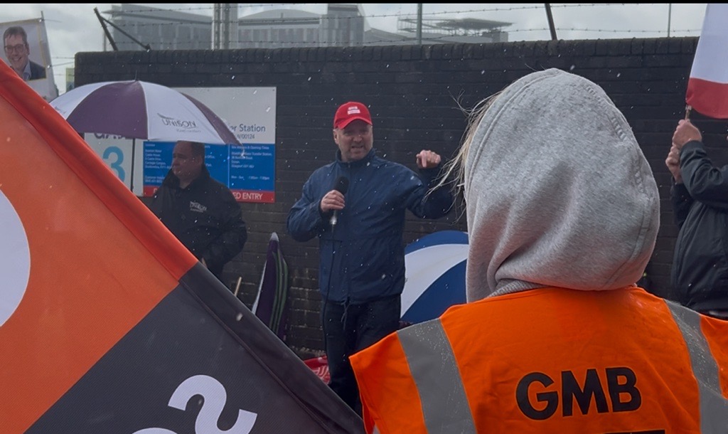 Gary Smith speaking into a mic in front of GMB members