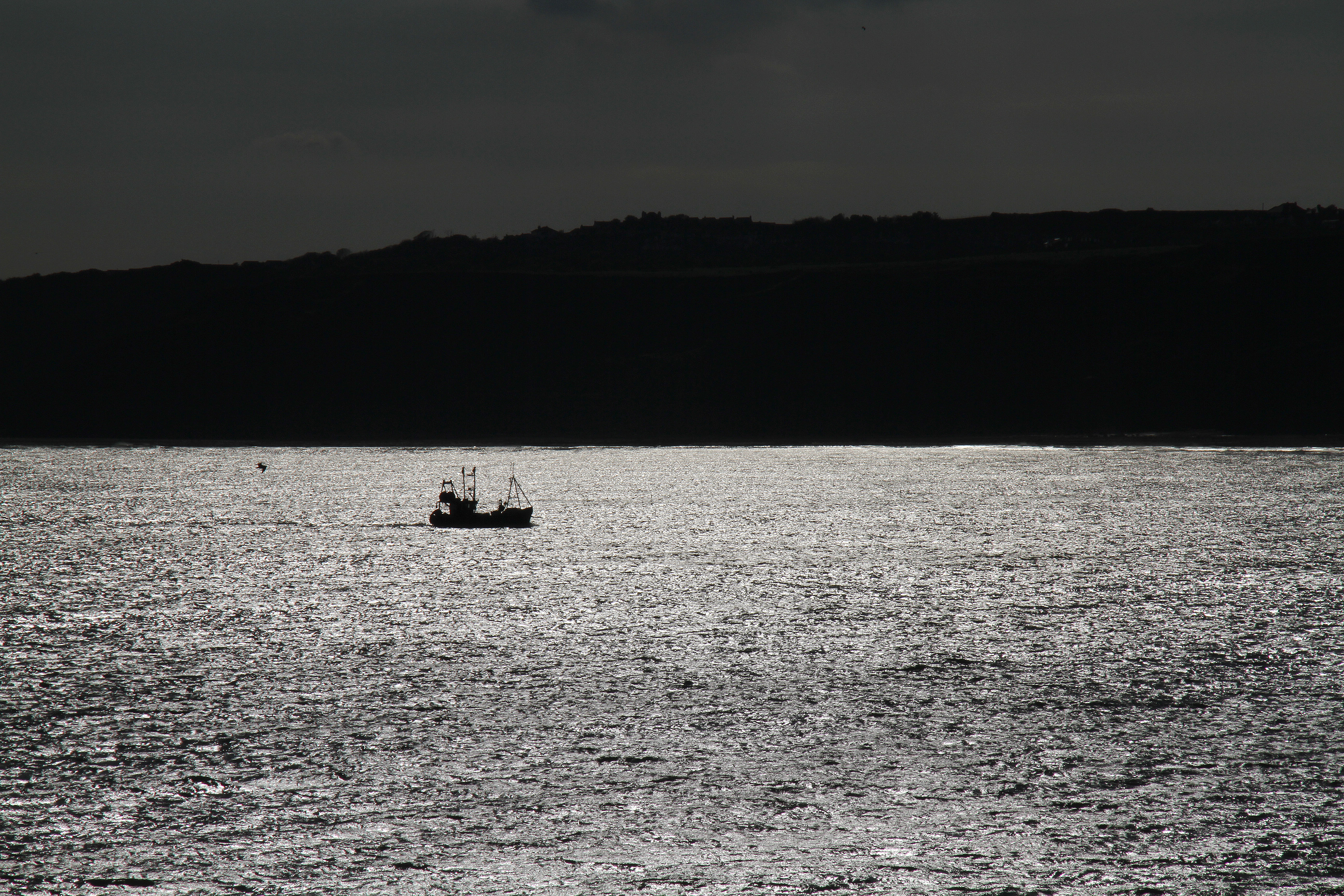 Fishing boat returning to harbour in silhouette