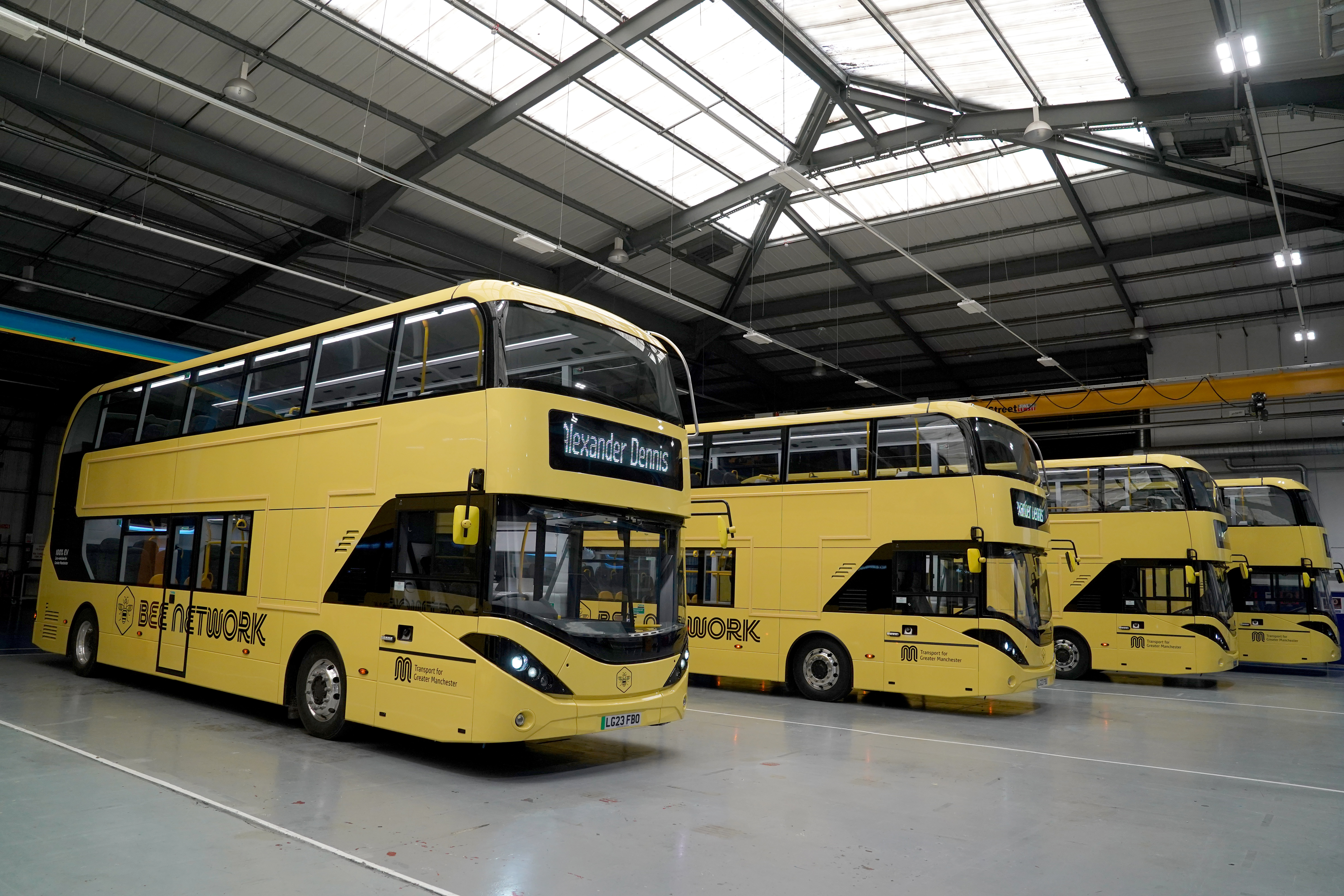 Four yellow Bee Network buses in a warehouse