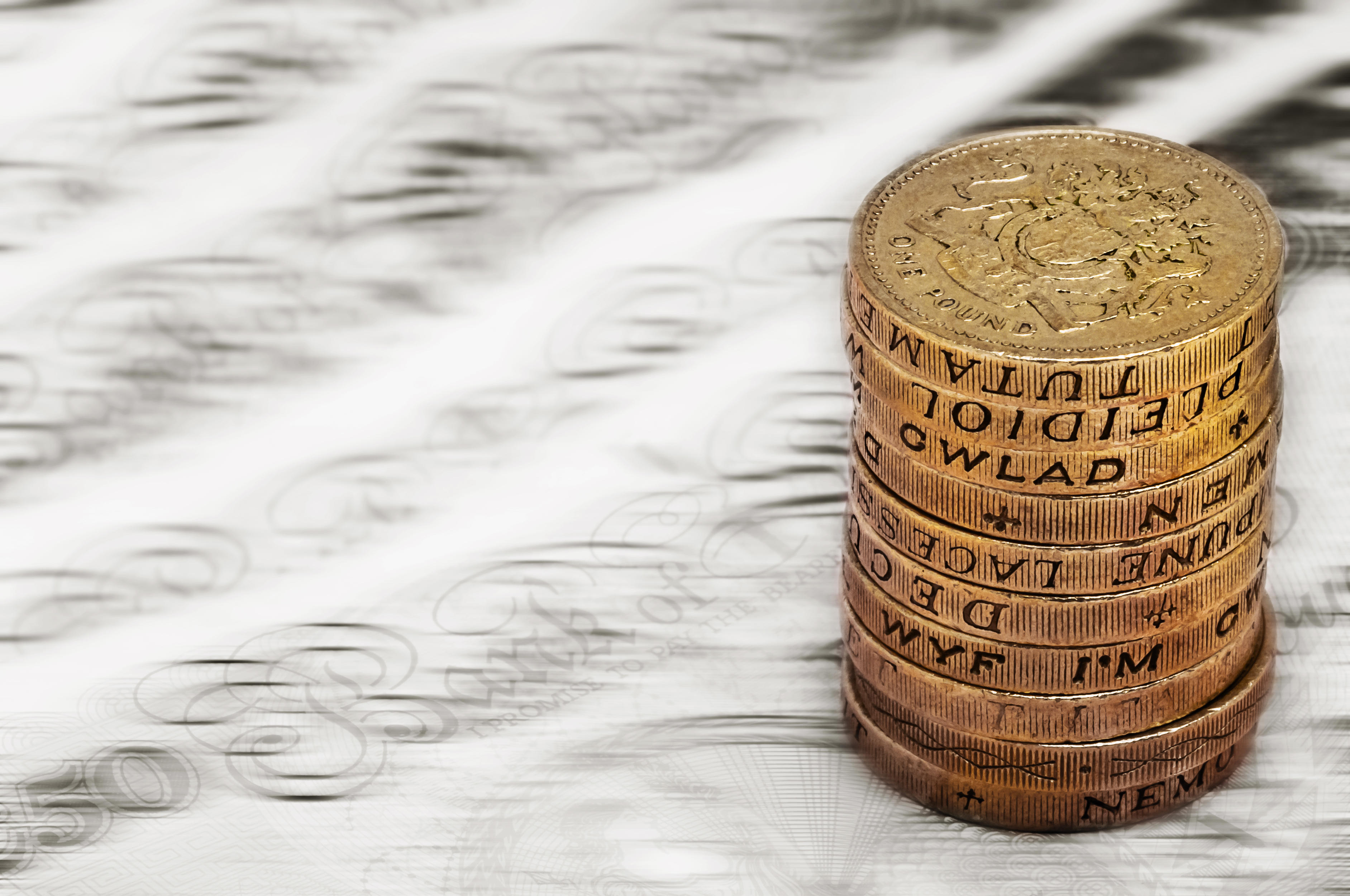 A pile of £1 coins sitting on banknotes, which are blurred