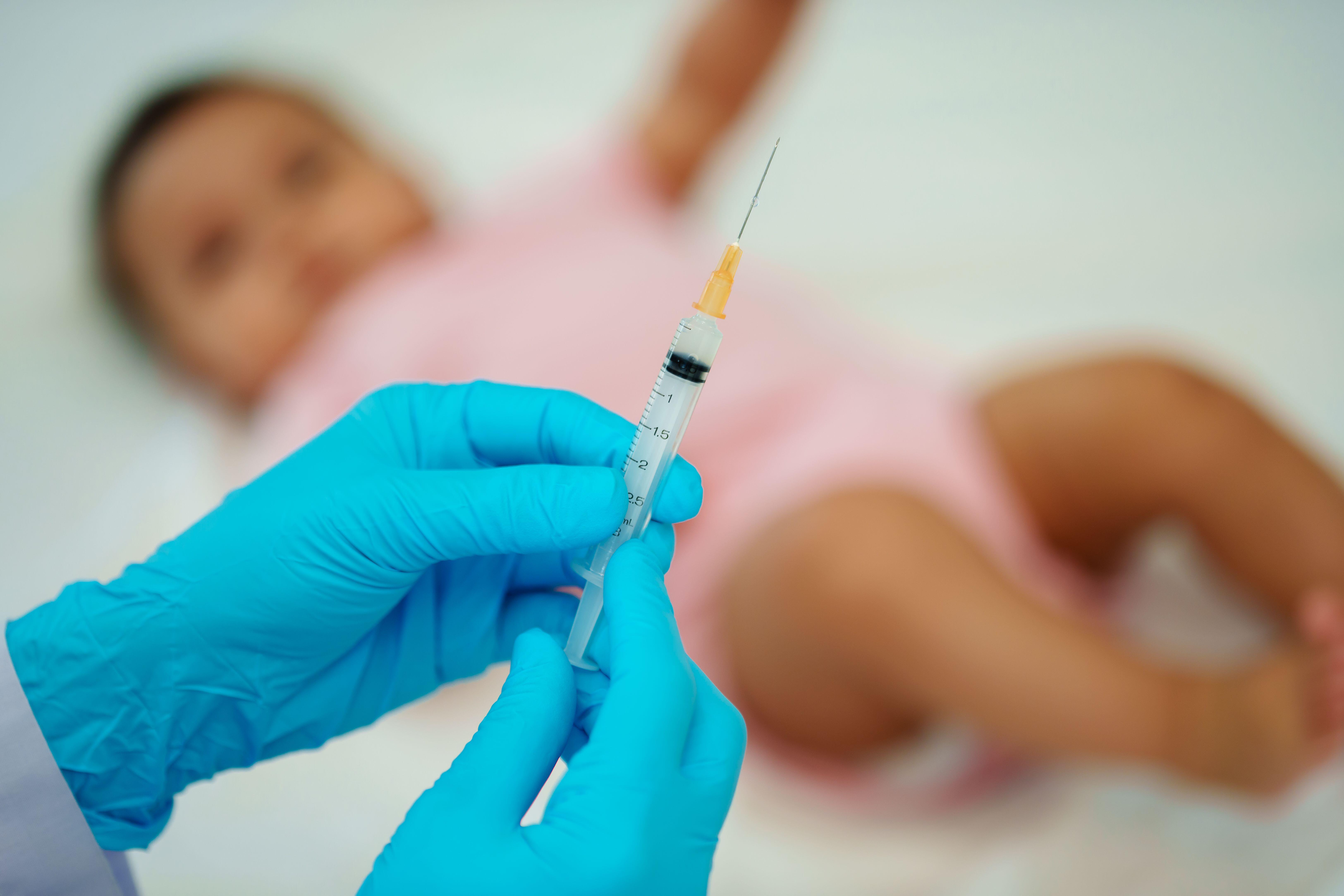 A doctor holding syringe and preparing vaccine giving injection to infant