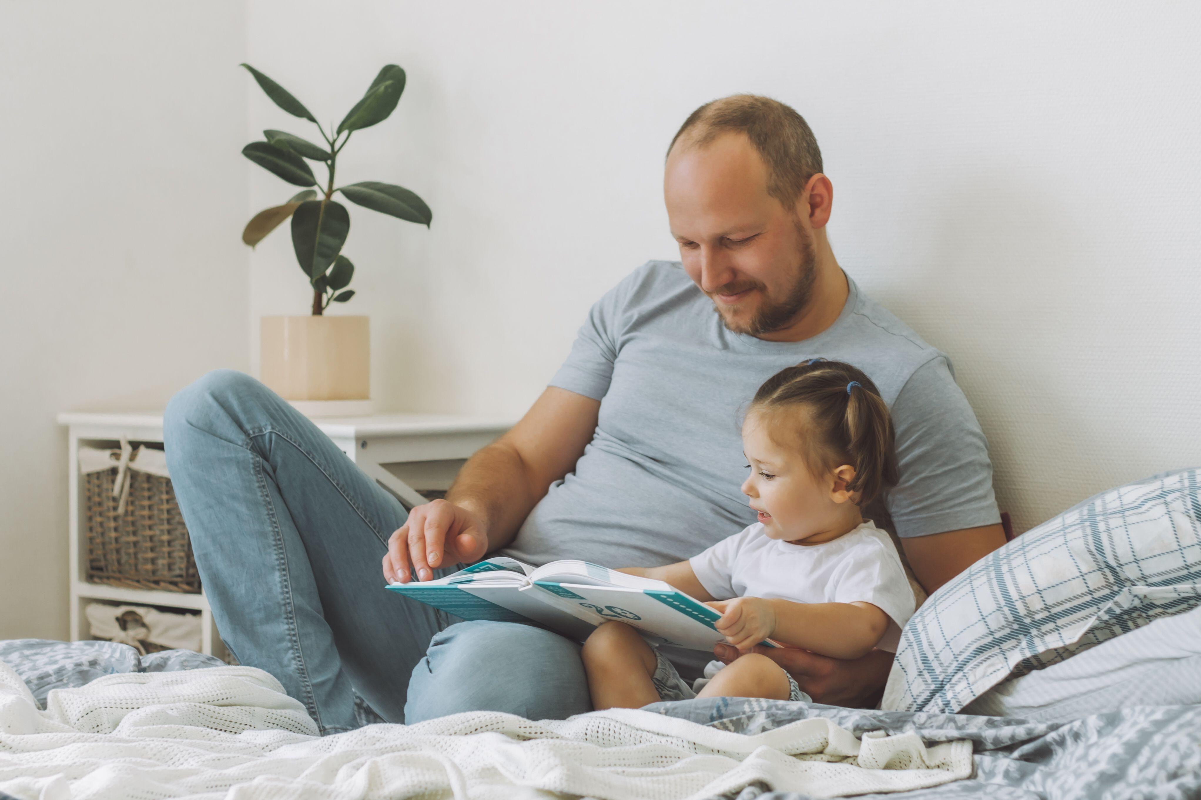 Little girl reading a book with her dad in bed