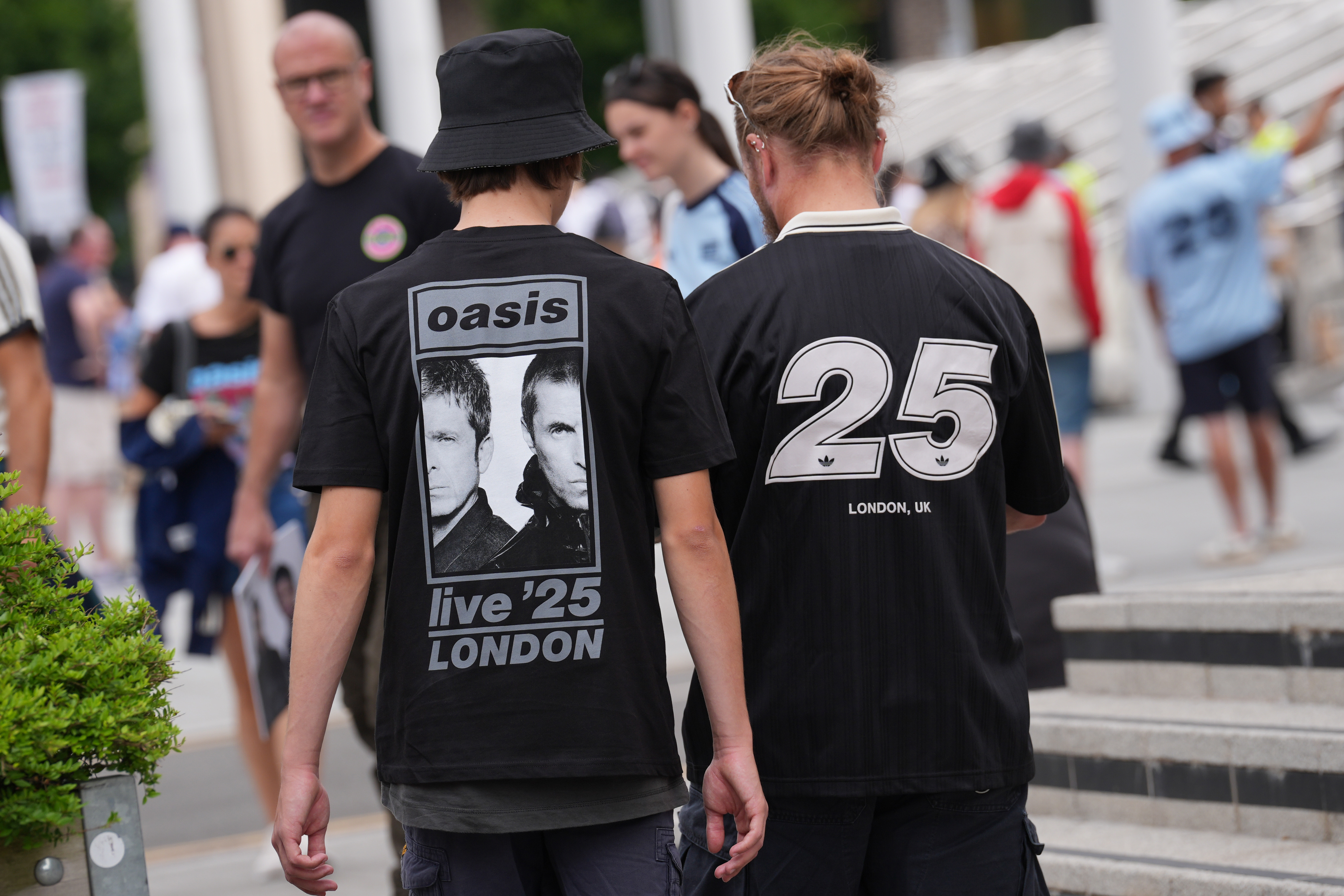 The backs of two Oasis fans, wearing band merchandise