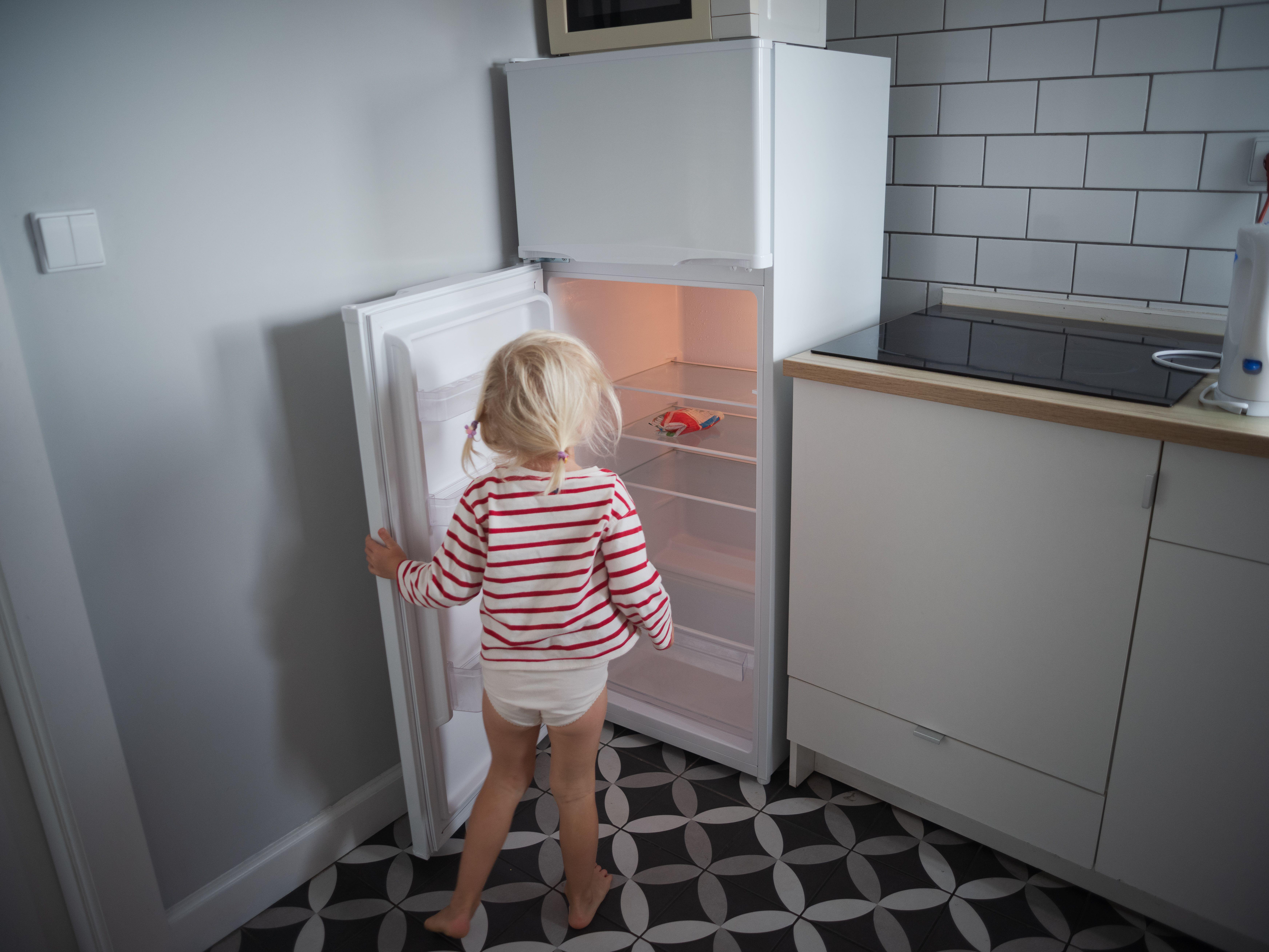 A little, hungry girl looking into an empty refrigerator at home