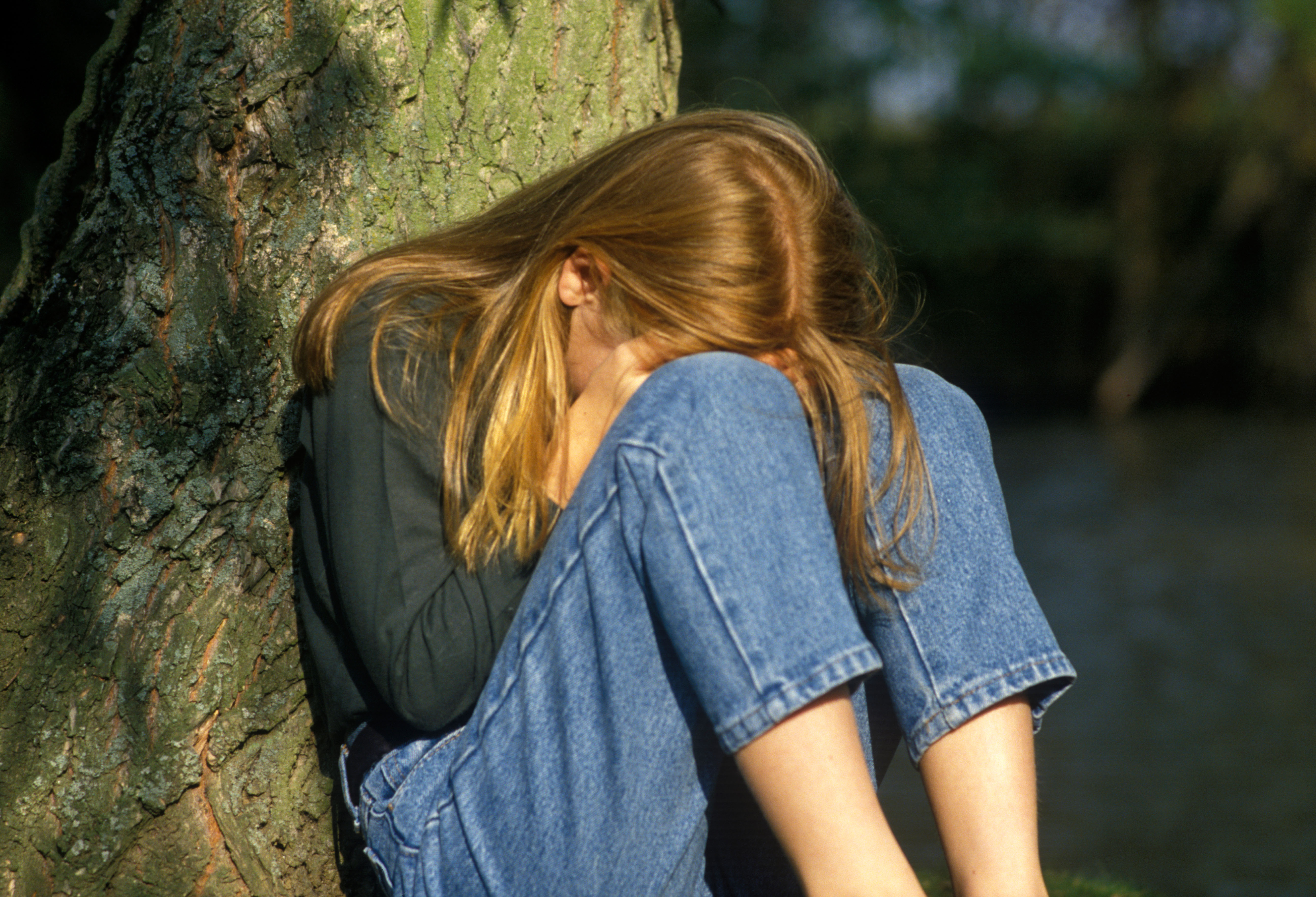 A distressed looking young girl sitting by a tree