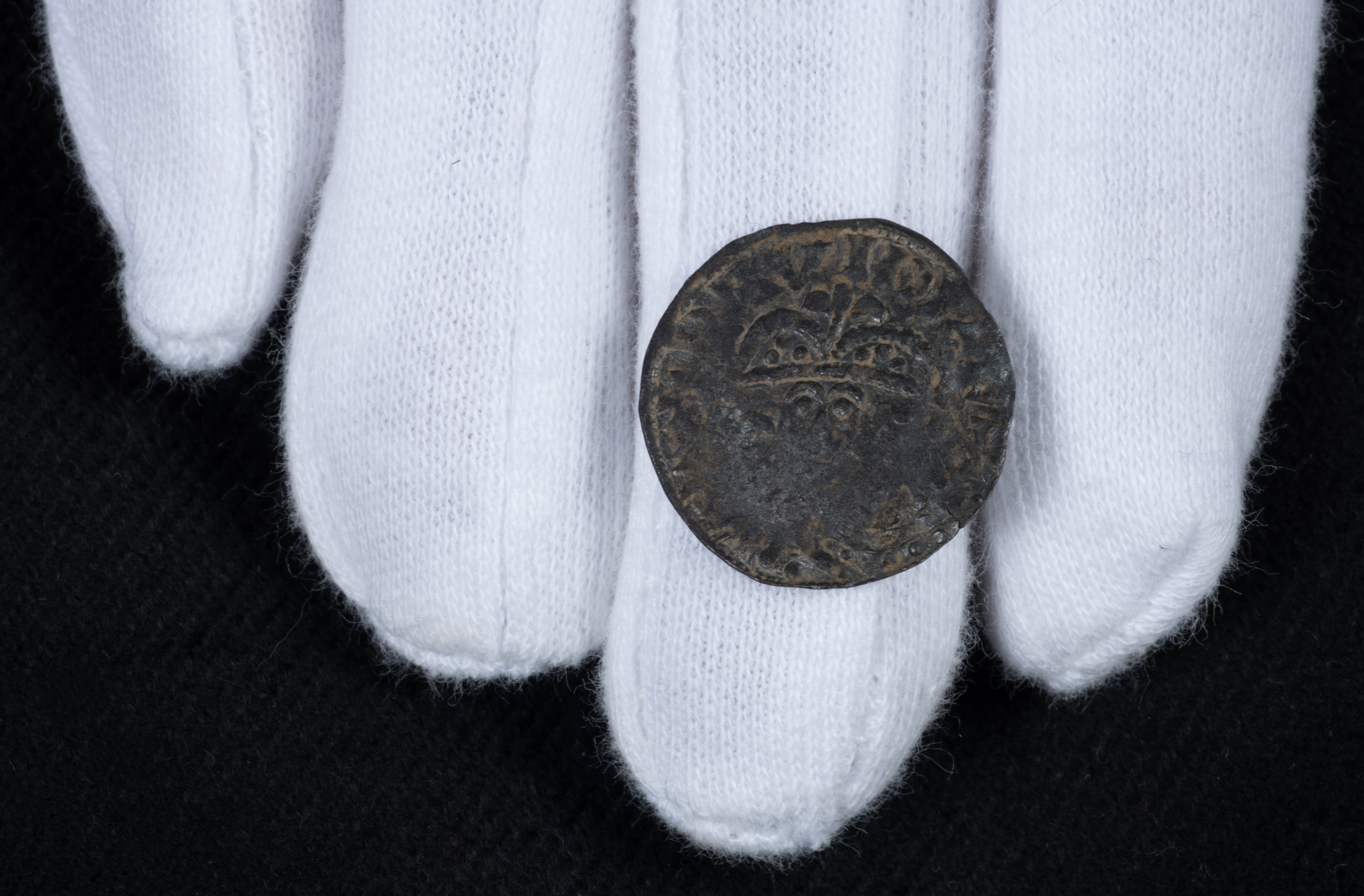 A medieval coin on the hands of a person wearing white gloves