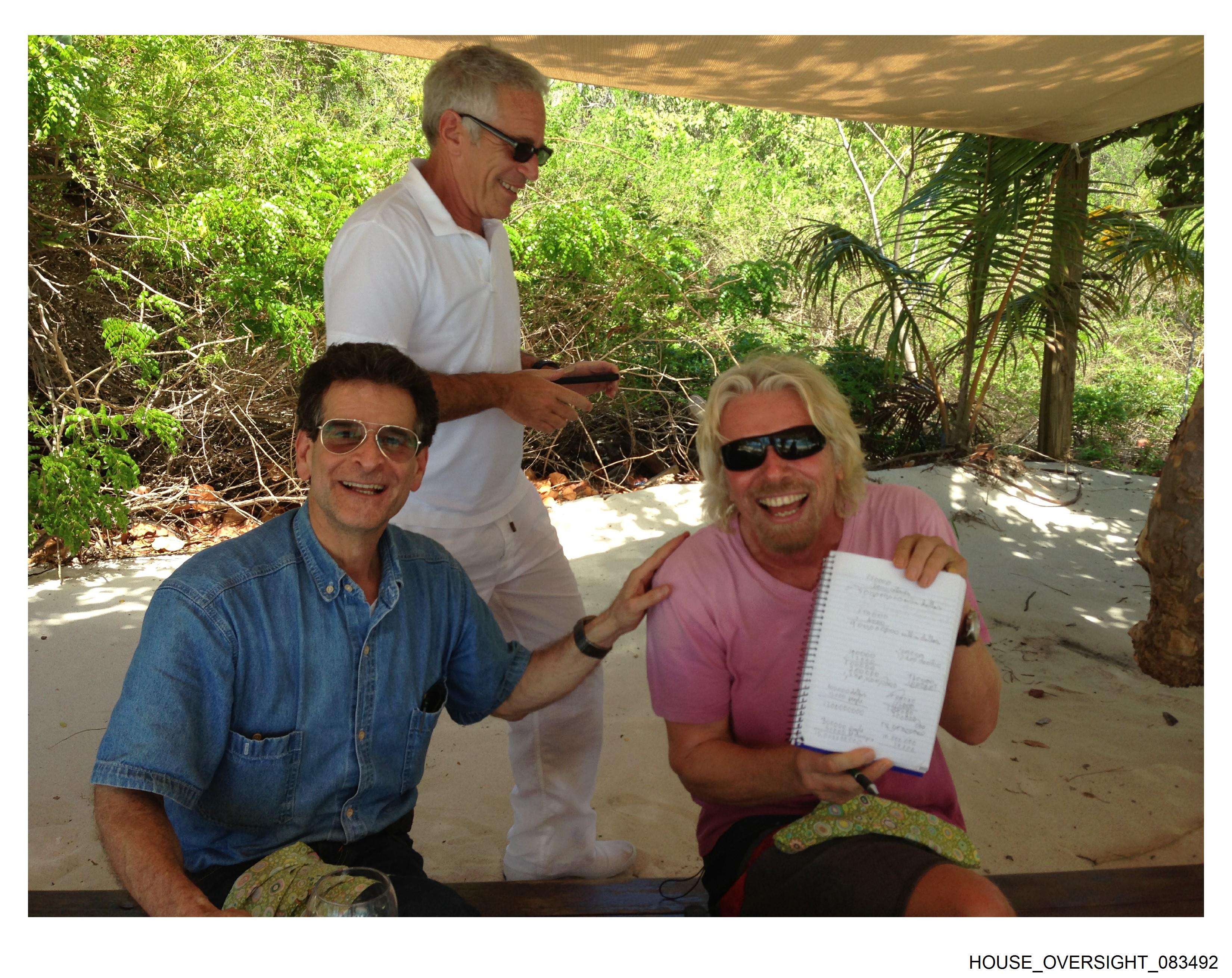 Sir Richard Branson on a beach holding up a notebook next to a man with Epstein standing behind them