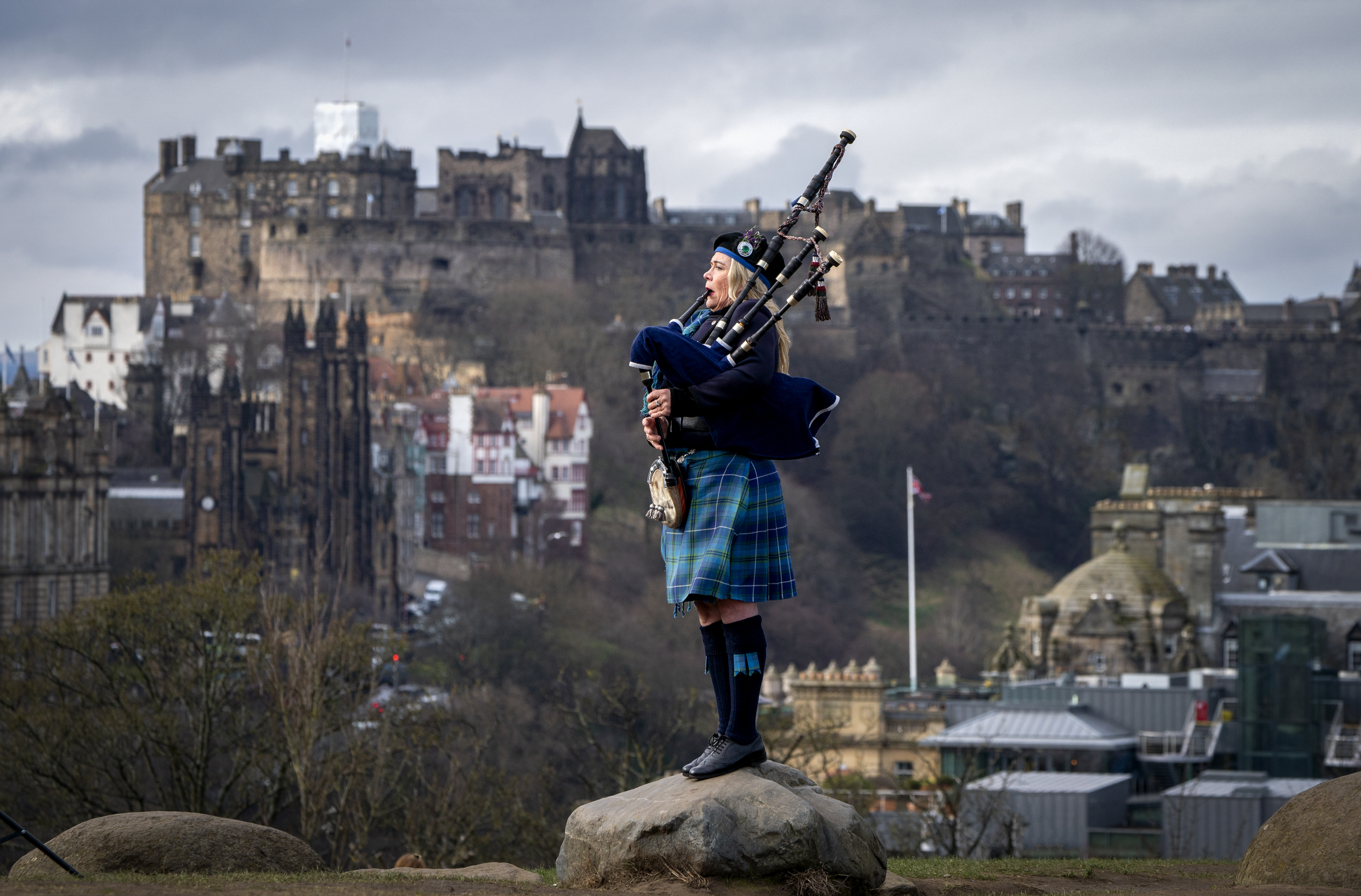 A bagpiper playing, with Edinburgh Castle in the background