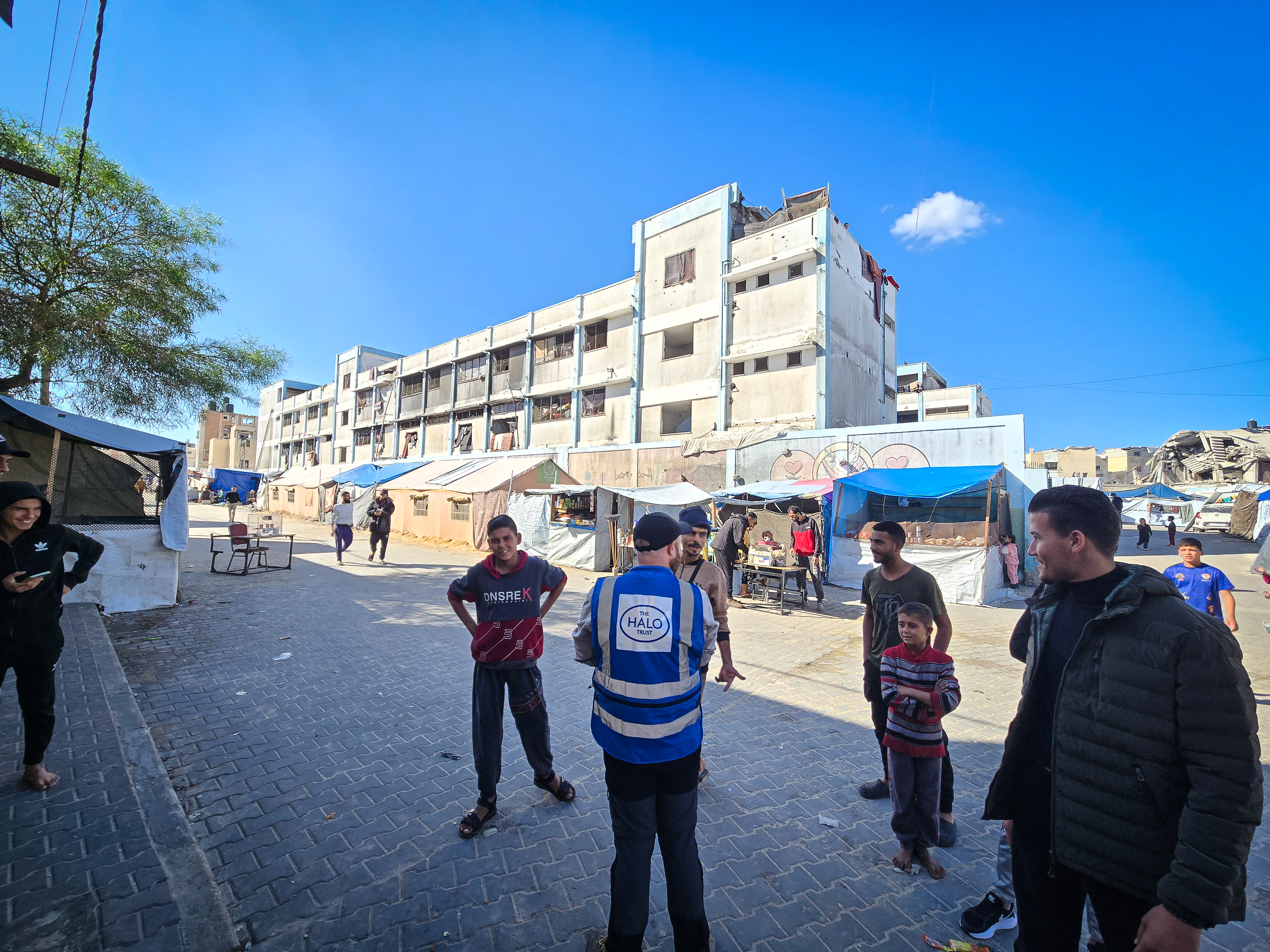 A person in a Halo Trust jacket among a group of Palestinians in an area of Gaza