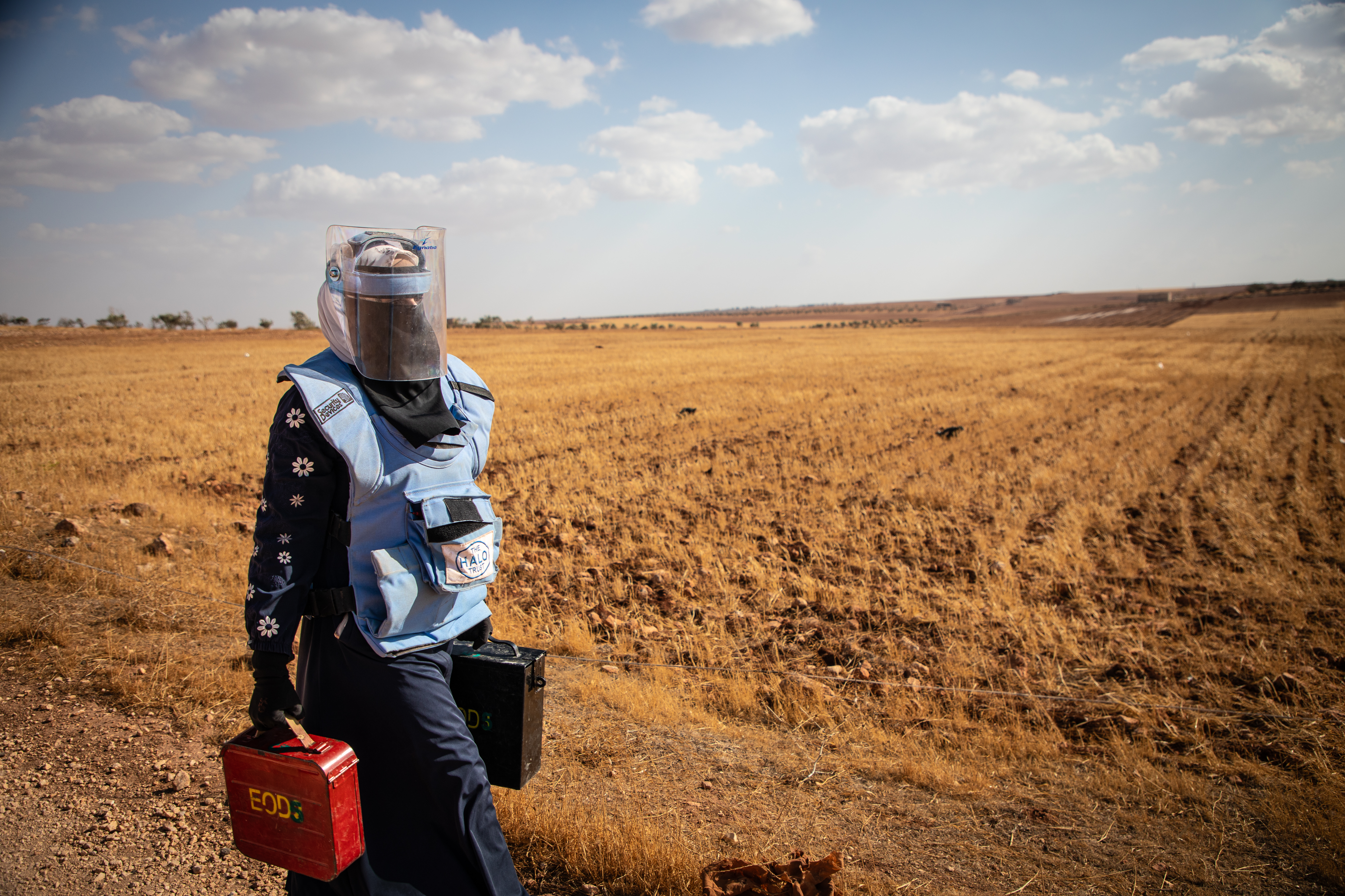 A Halo Trust worker in protective gear walking alongside a field