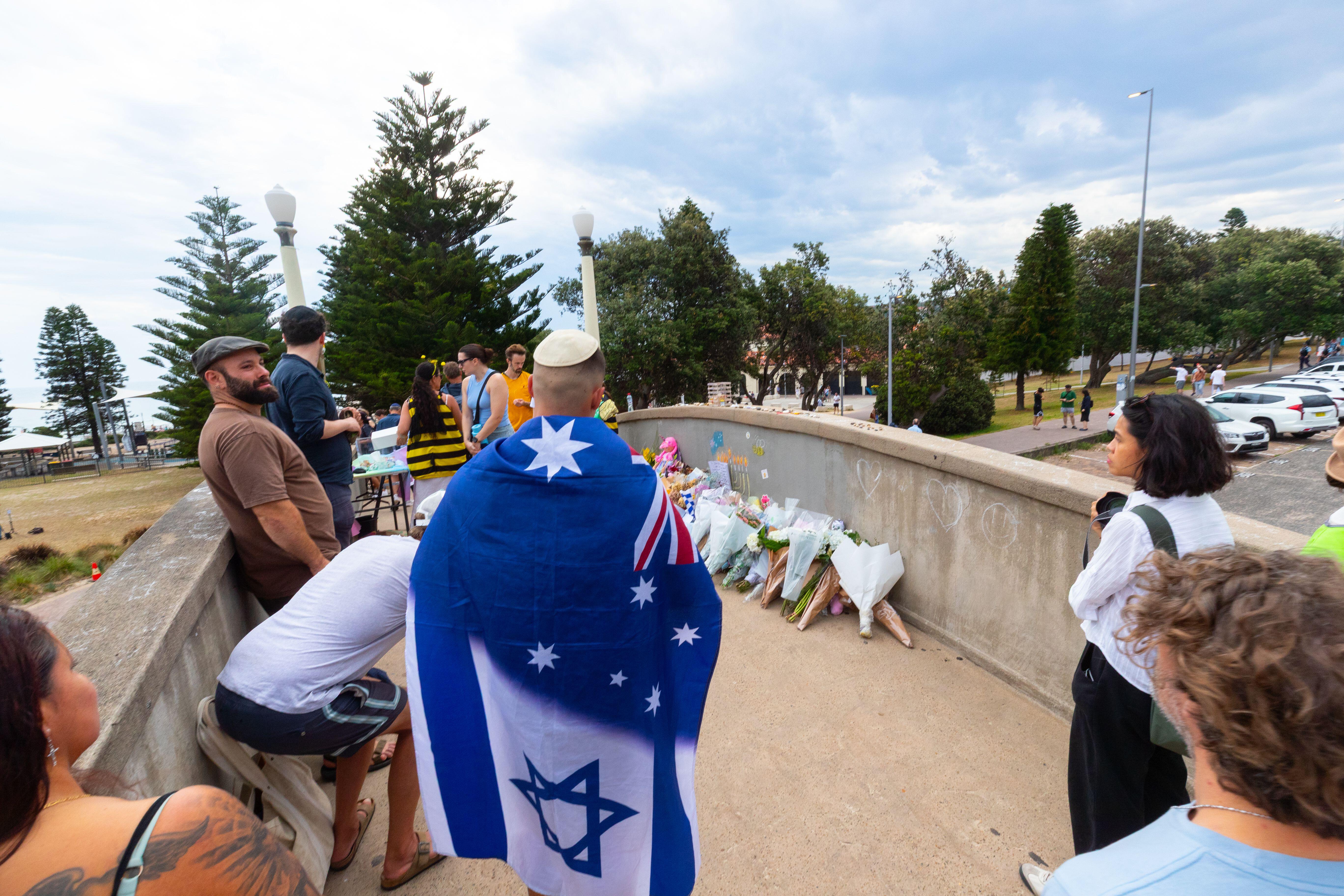 People, including one draped in flags look at flowers on the footbridge 