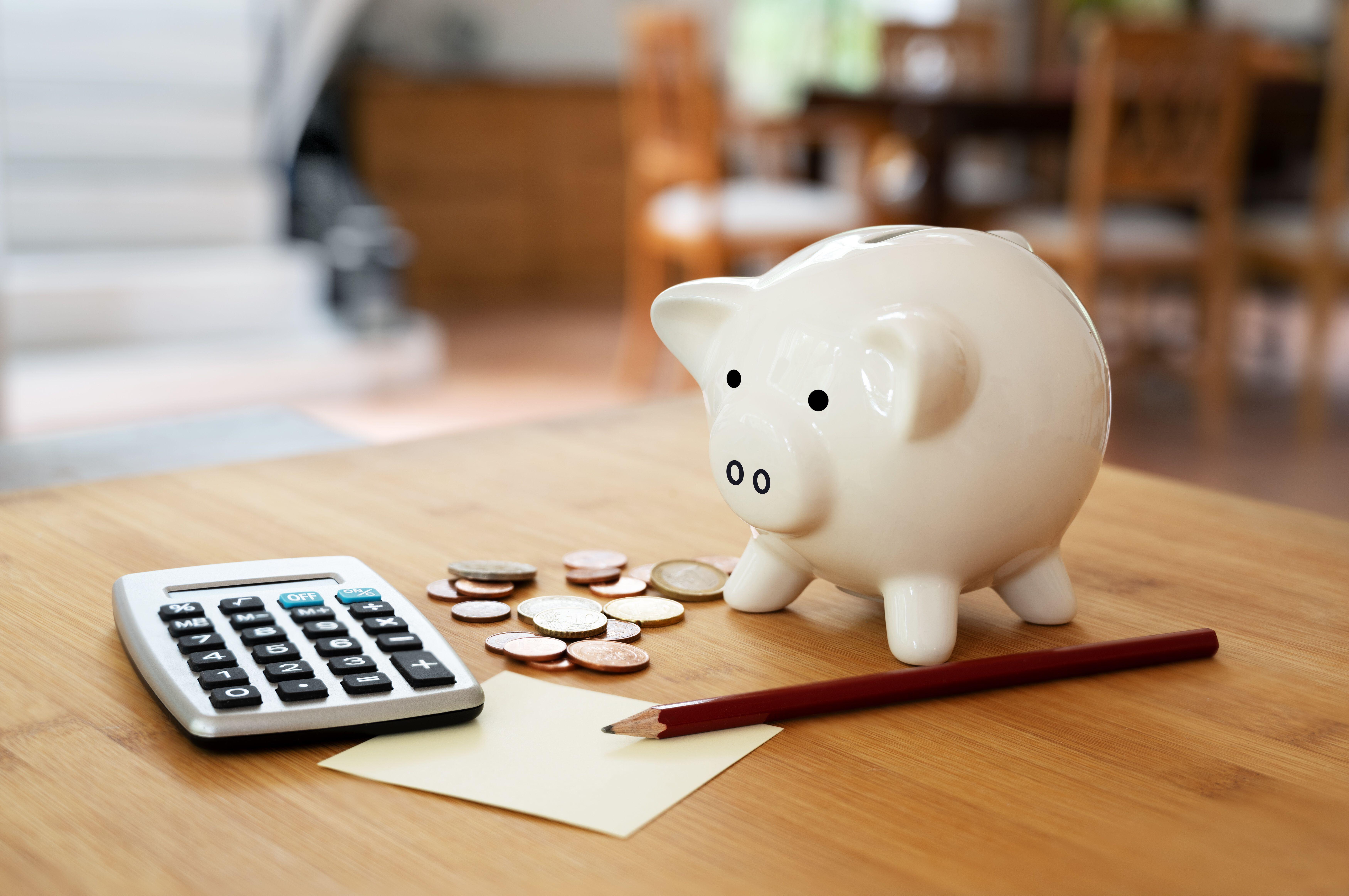 A calculator with coins, pencil and a piggy bank on a table