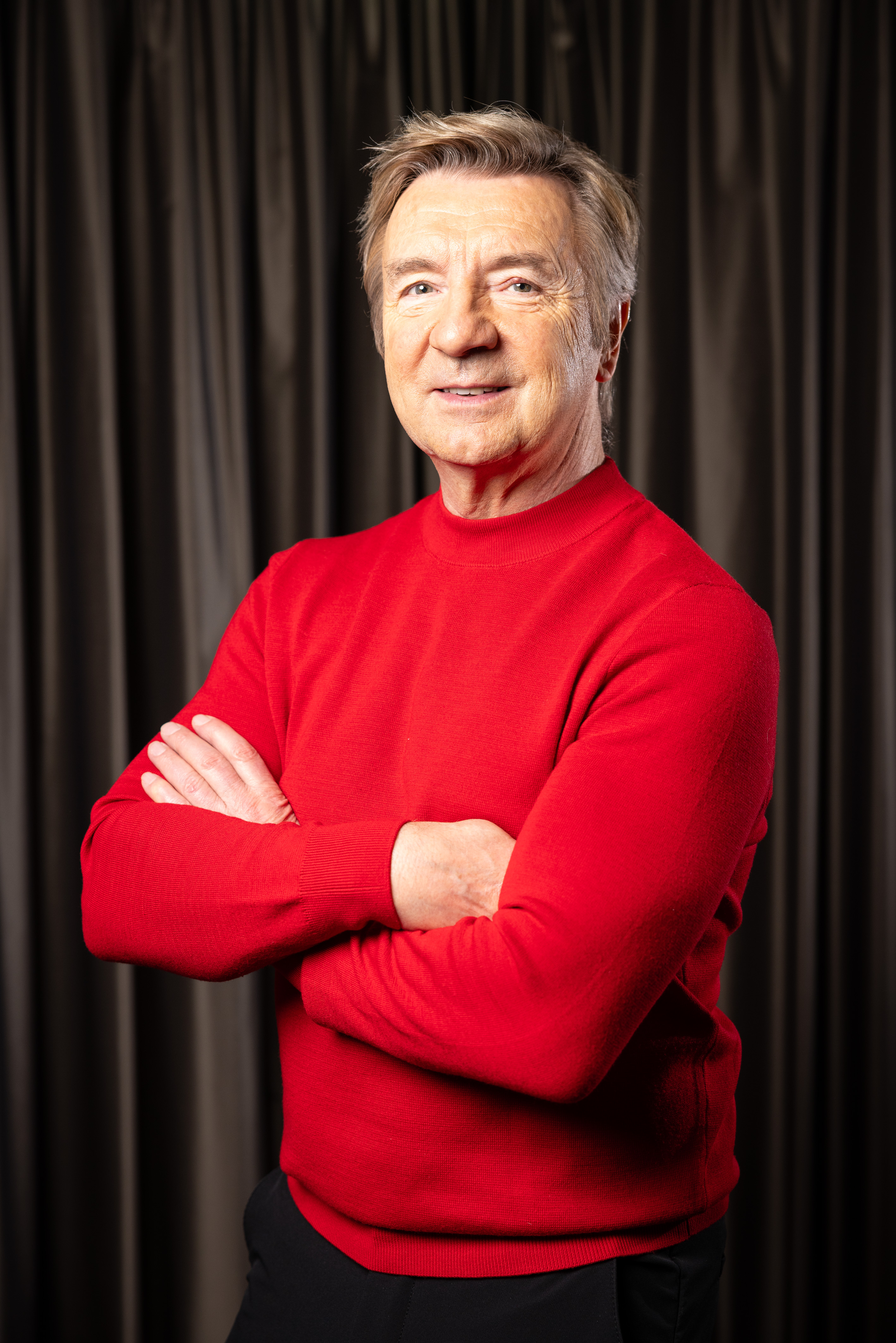 Sir Christopher Dean wearing a red jumper with his arms folded