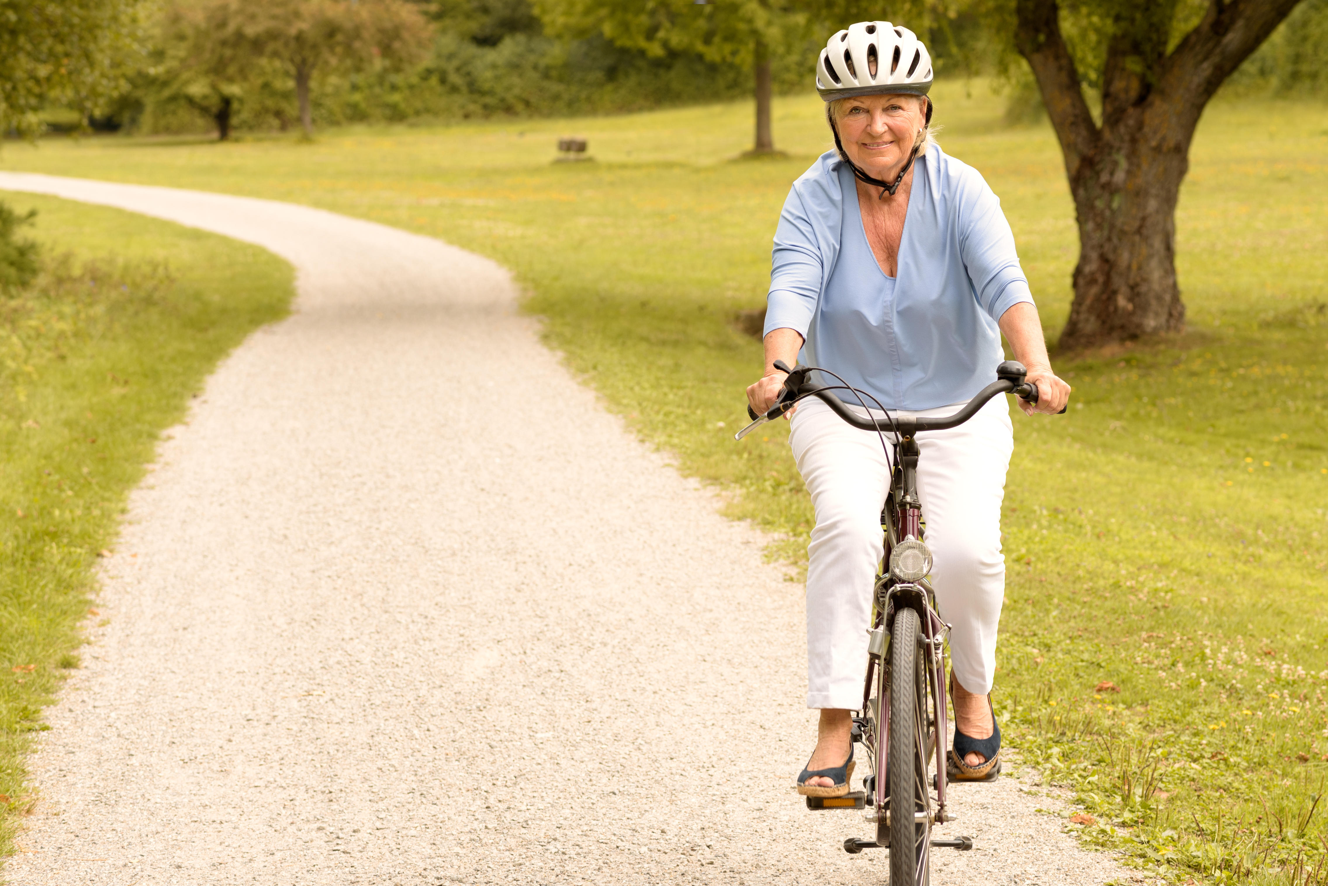 Fit healthy senior lady out cycling on her bicycle on a country road wearing a protective helmet and smiling happily at the came