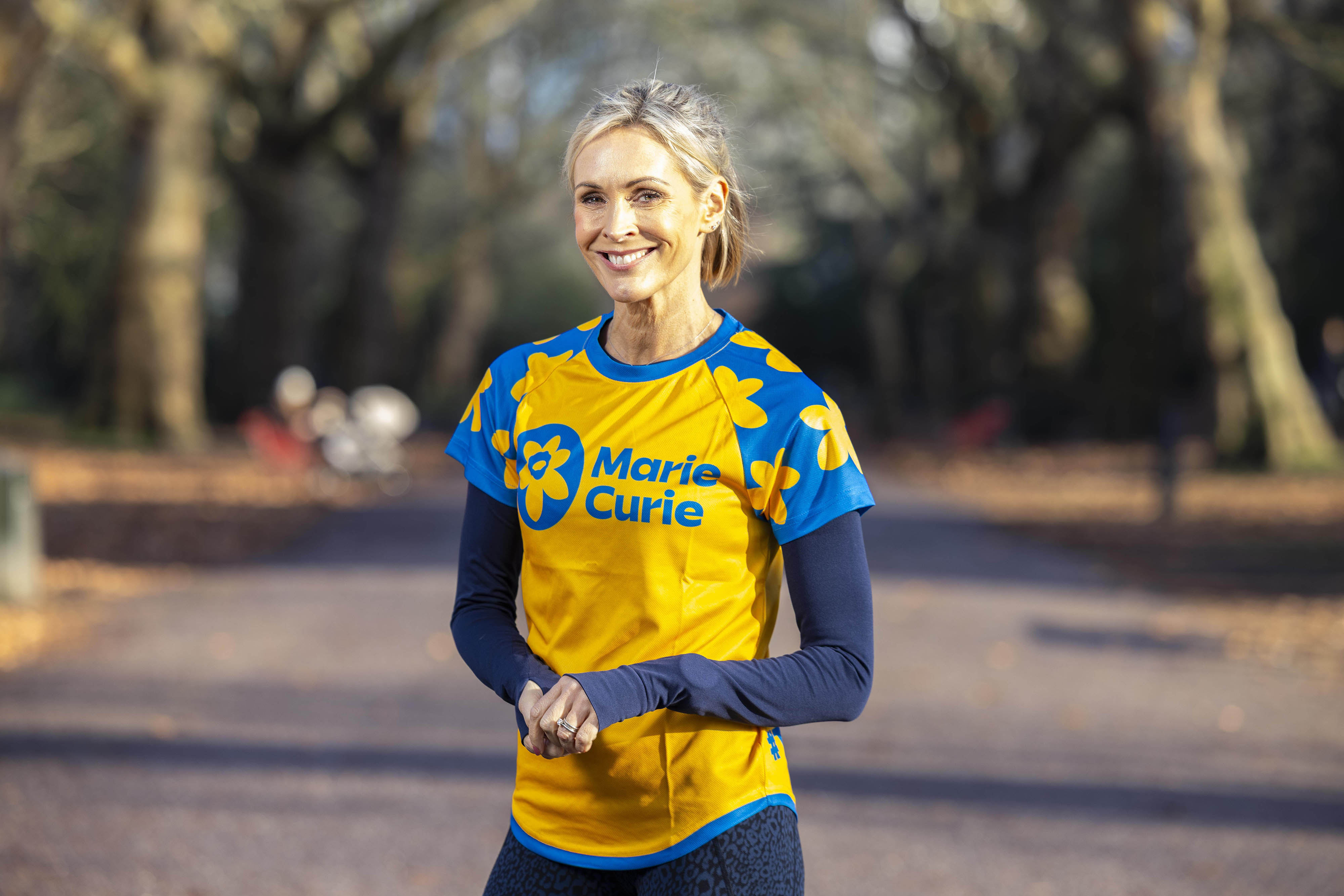 Jenni Falconer smiling while wearing a Marie Curie T-shirt and running gear in a park