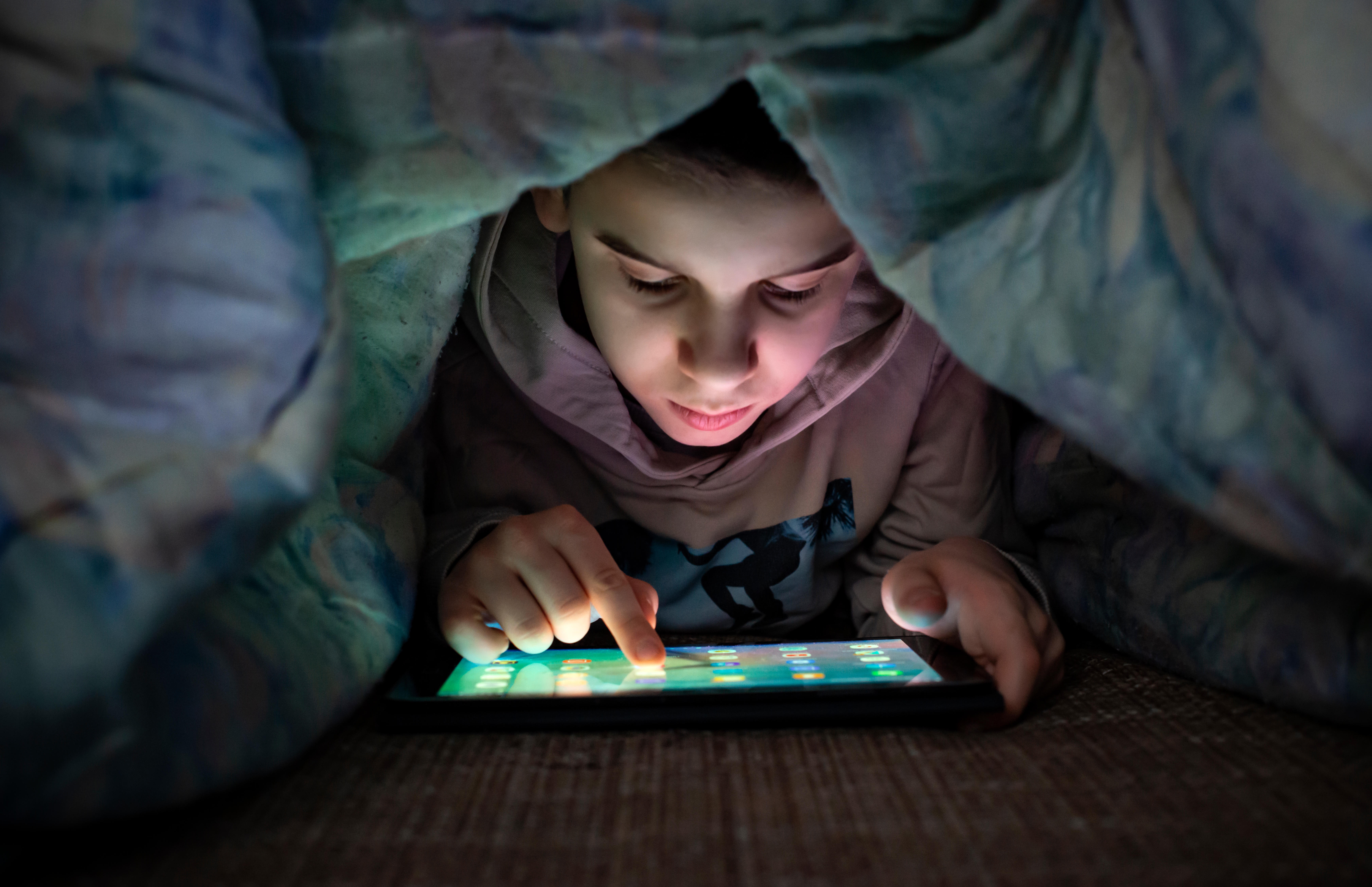 Child watching his tablet in the bed under the covers