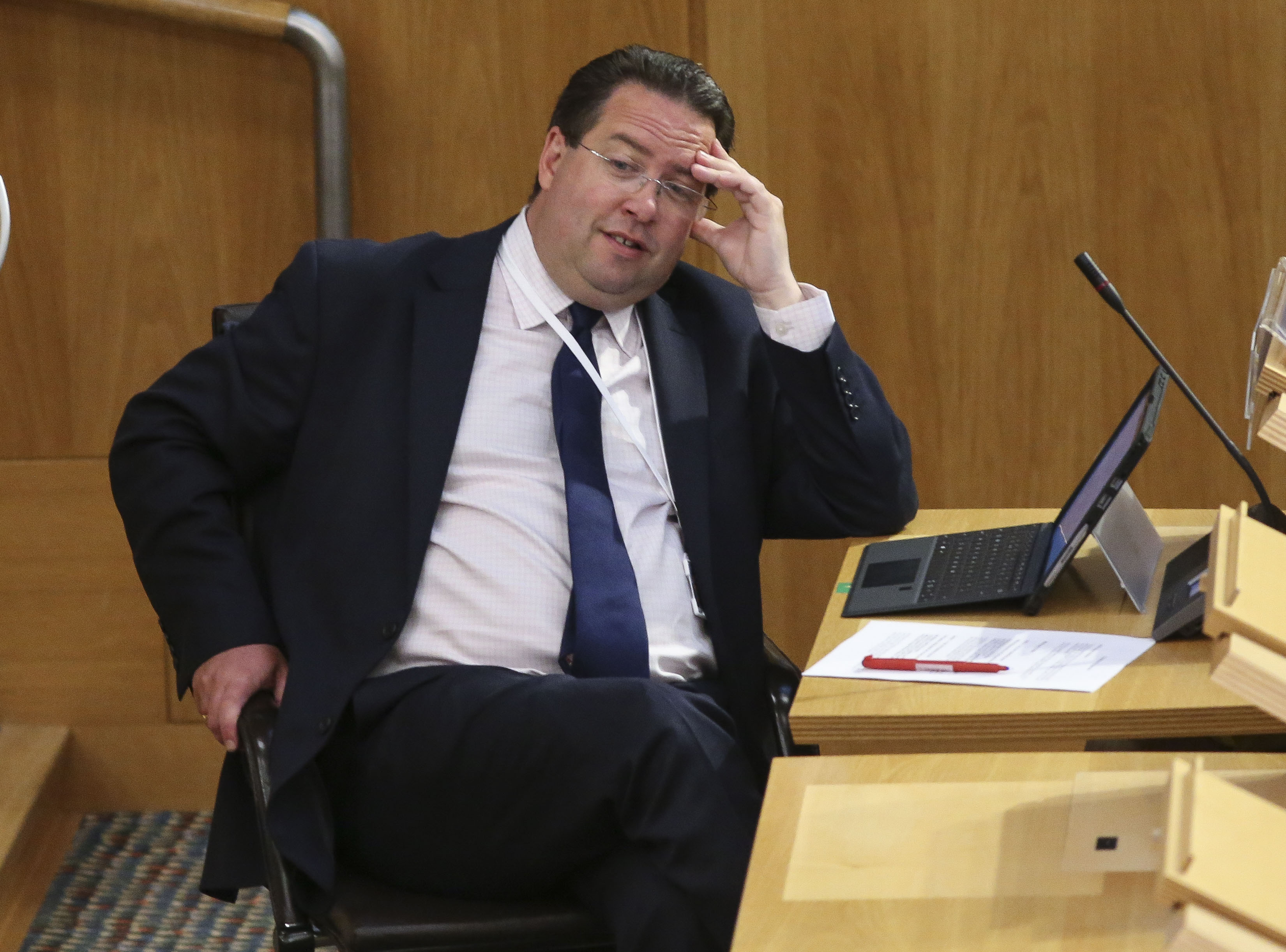 Craig Hoy seated in Parliament, with one hand resting on his forehead