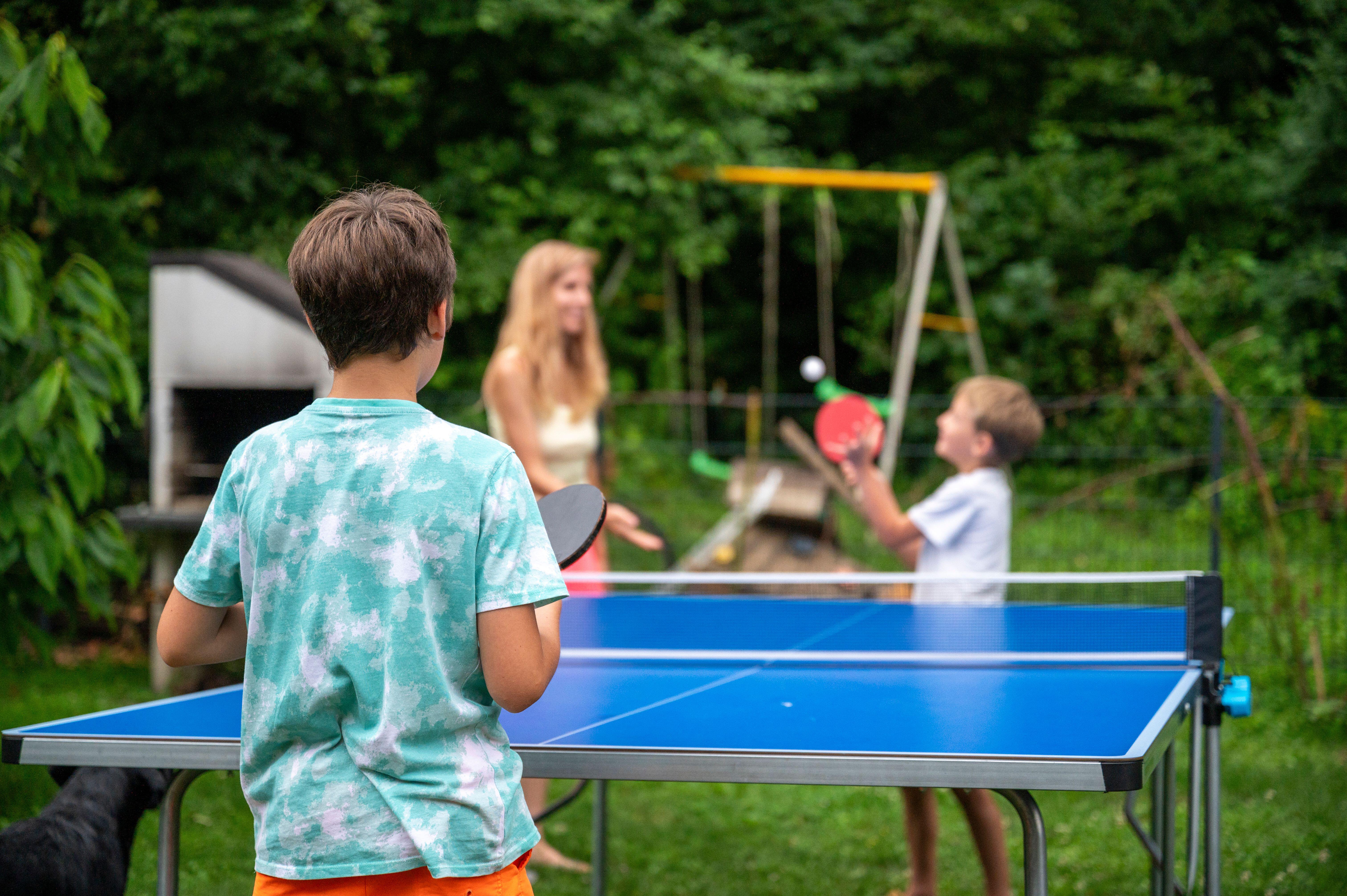  Two brothers and their mother enjoy a lively table tennis game in a lush backyard setting