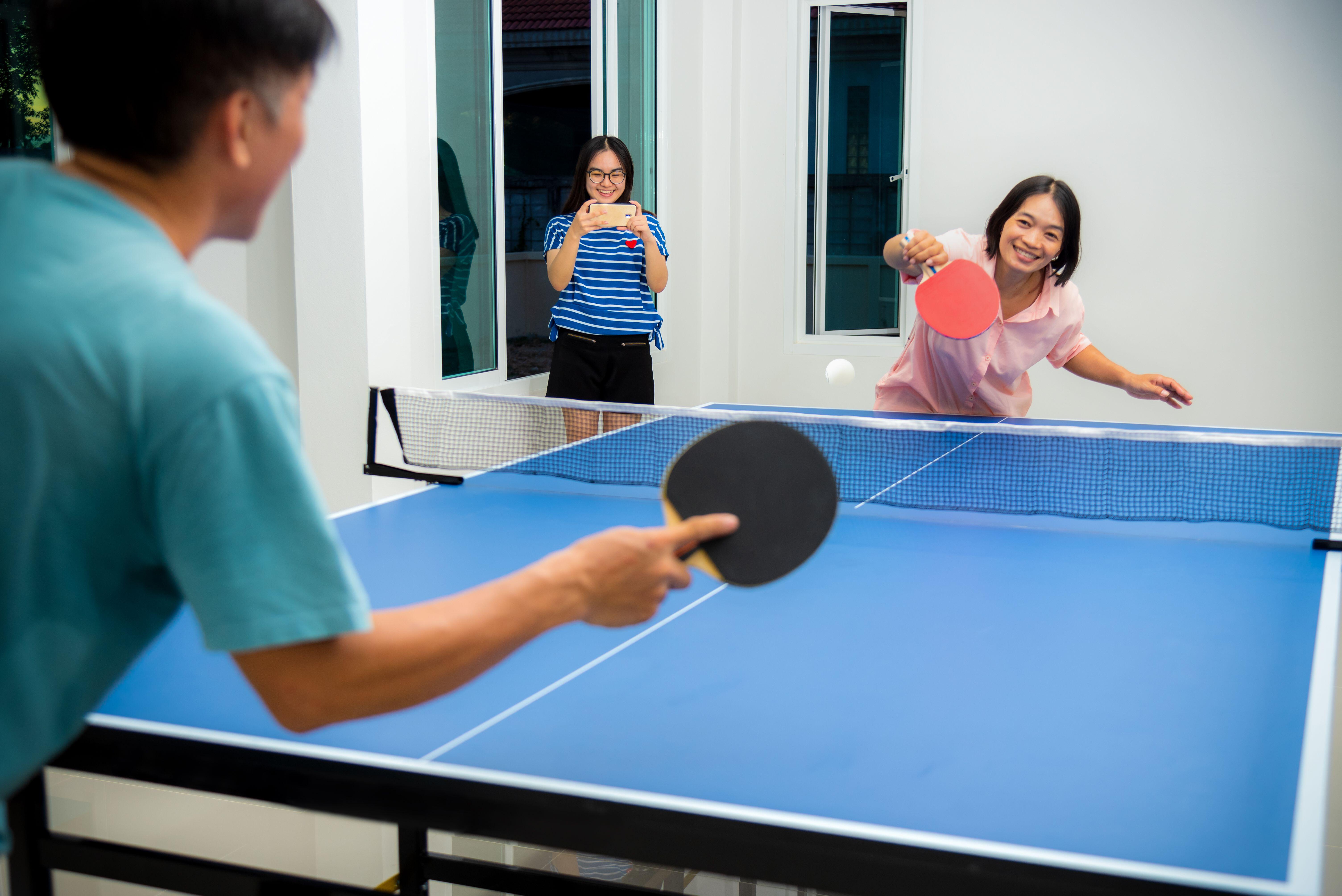 Couple fun playing table tennis outside while daughter films them on her phone