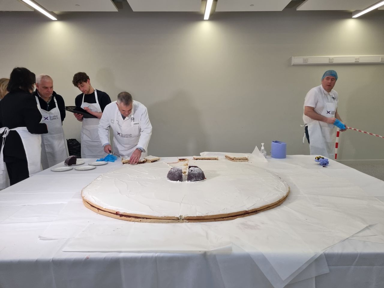 A baker cuts into a giant Empire biscuit, while judges stand nearby