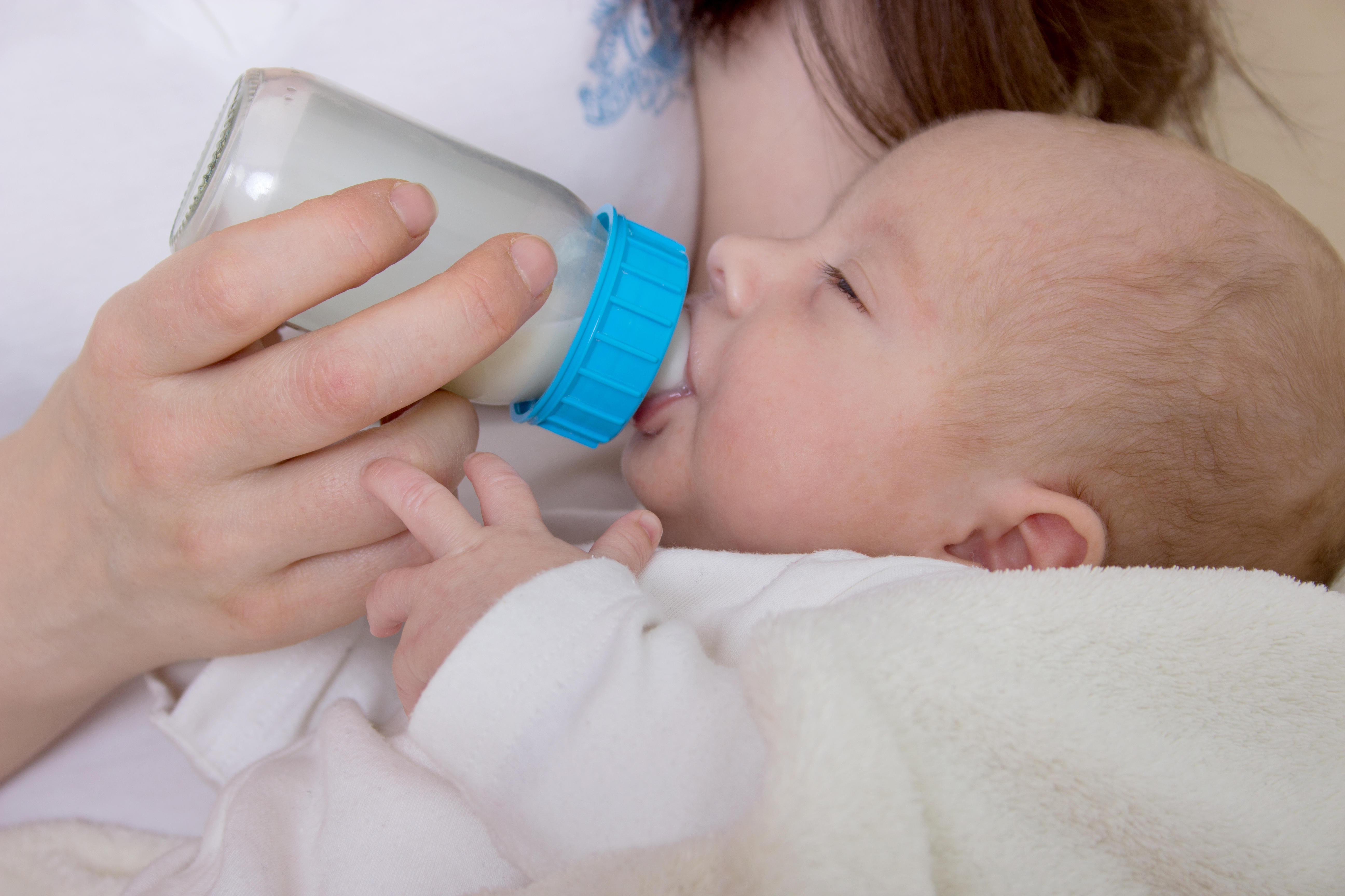 A baby in the arms of a woman drinking from a bottle