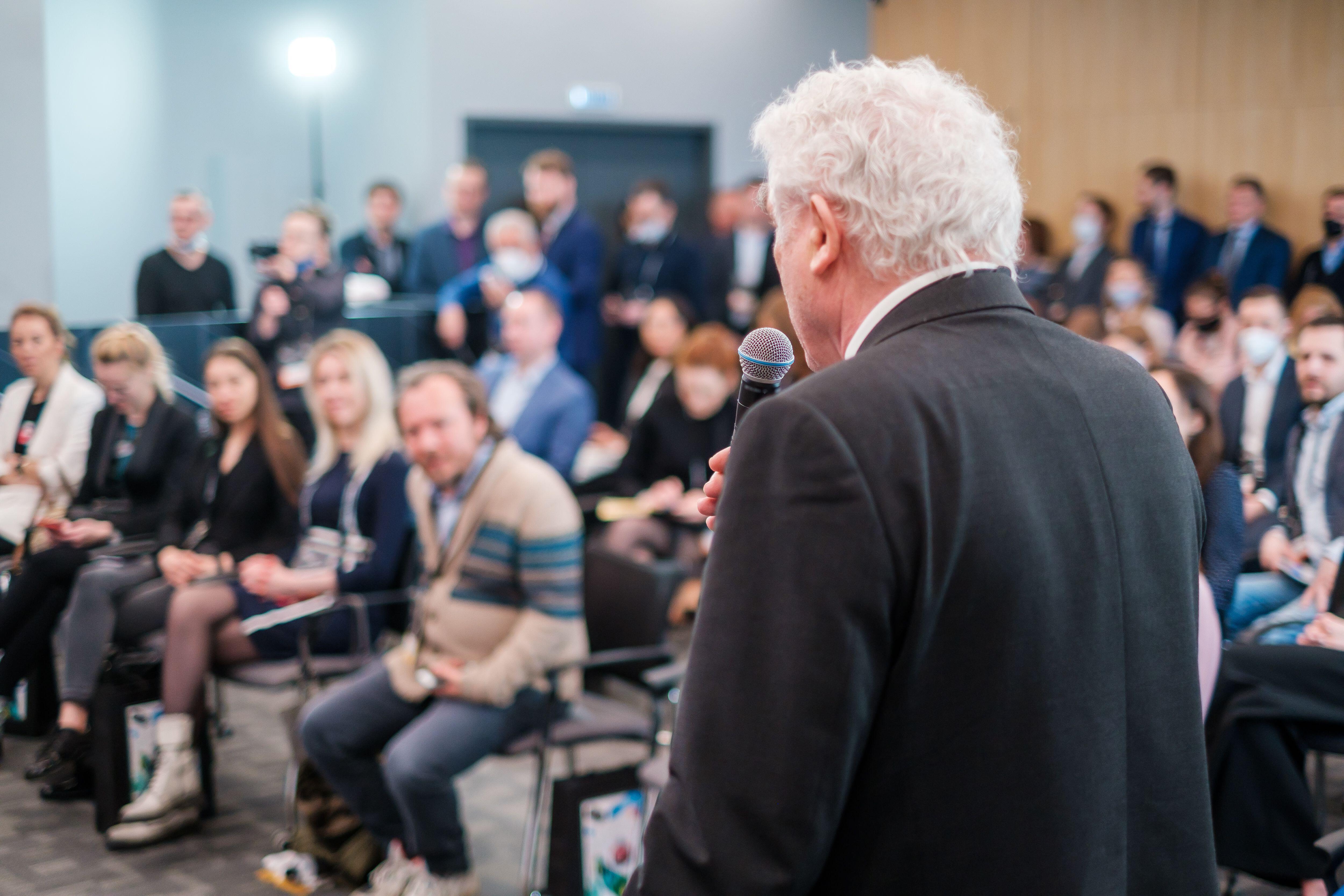 An elderly man speaking into a microphone in front of an audience