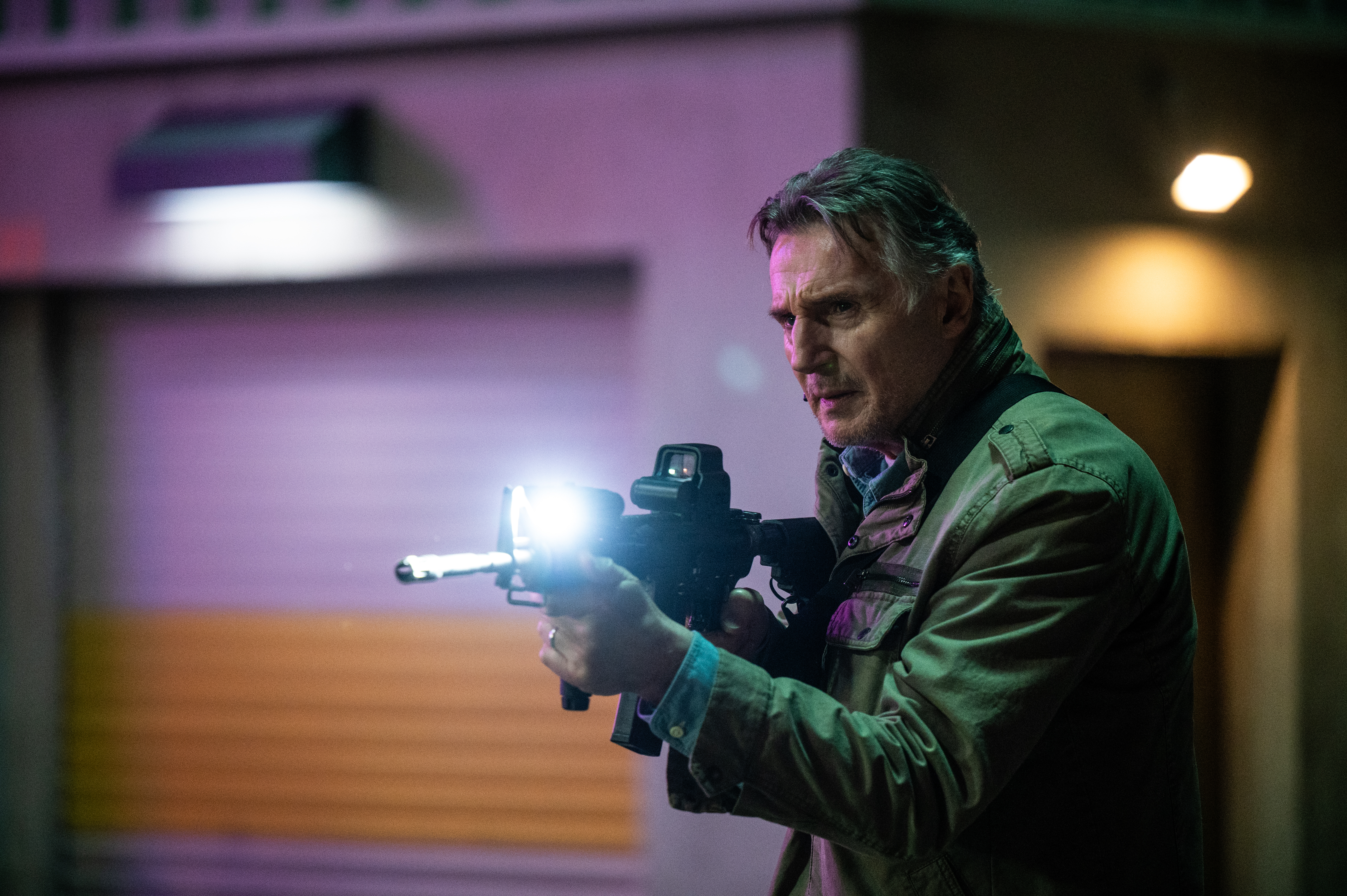 Liam Neeson in character, holding a gun