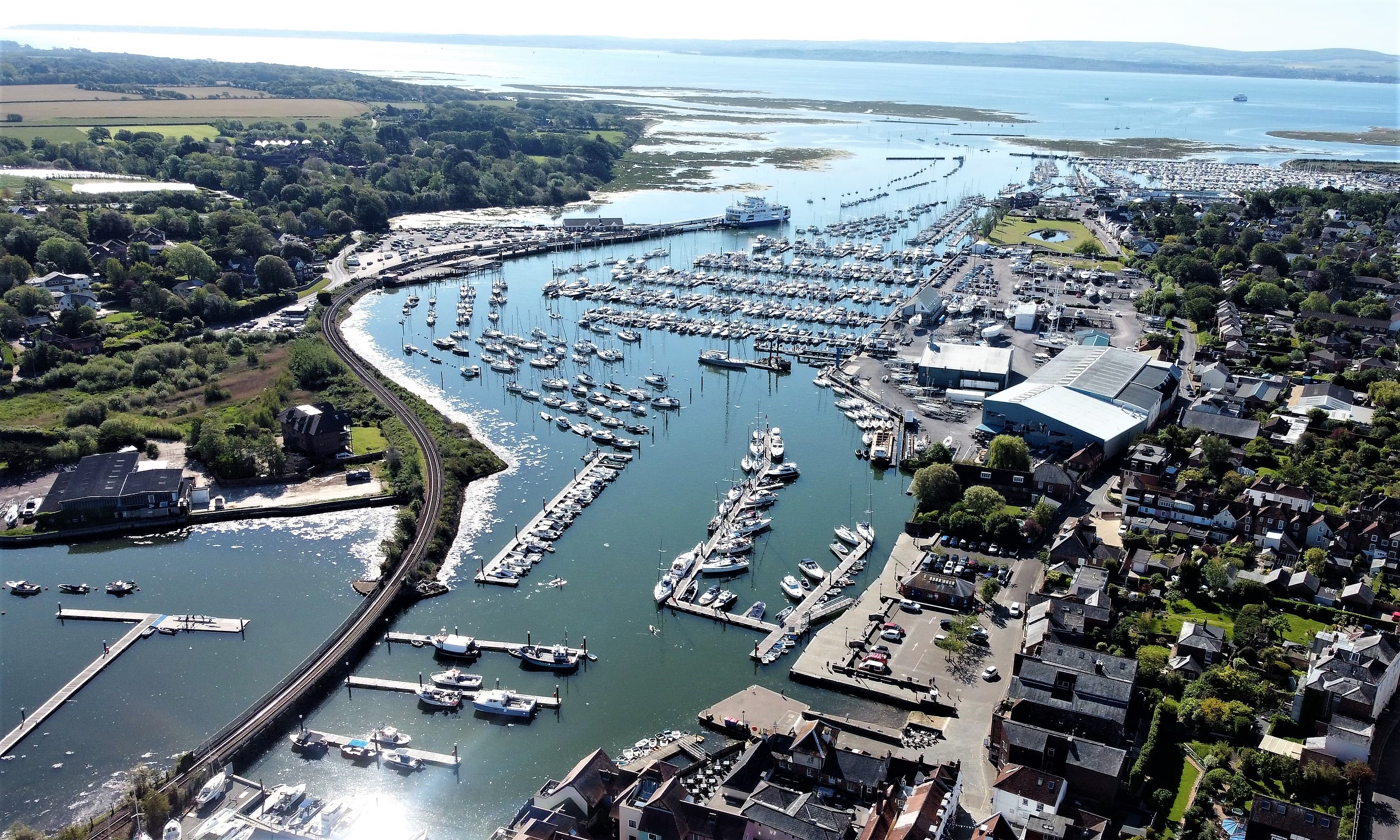 An aerial view of Lymington Harbour, showing moored yachts, buildings and in the distance, the saltmarsh protecting the harbour.
