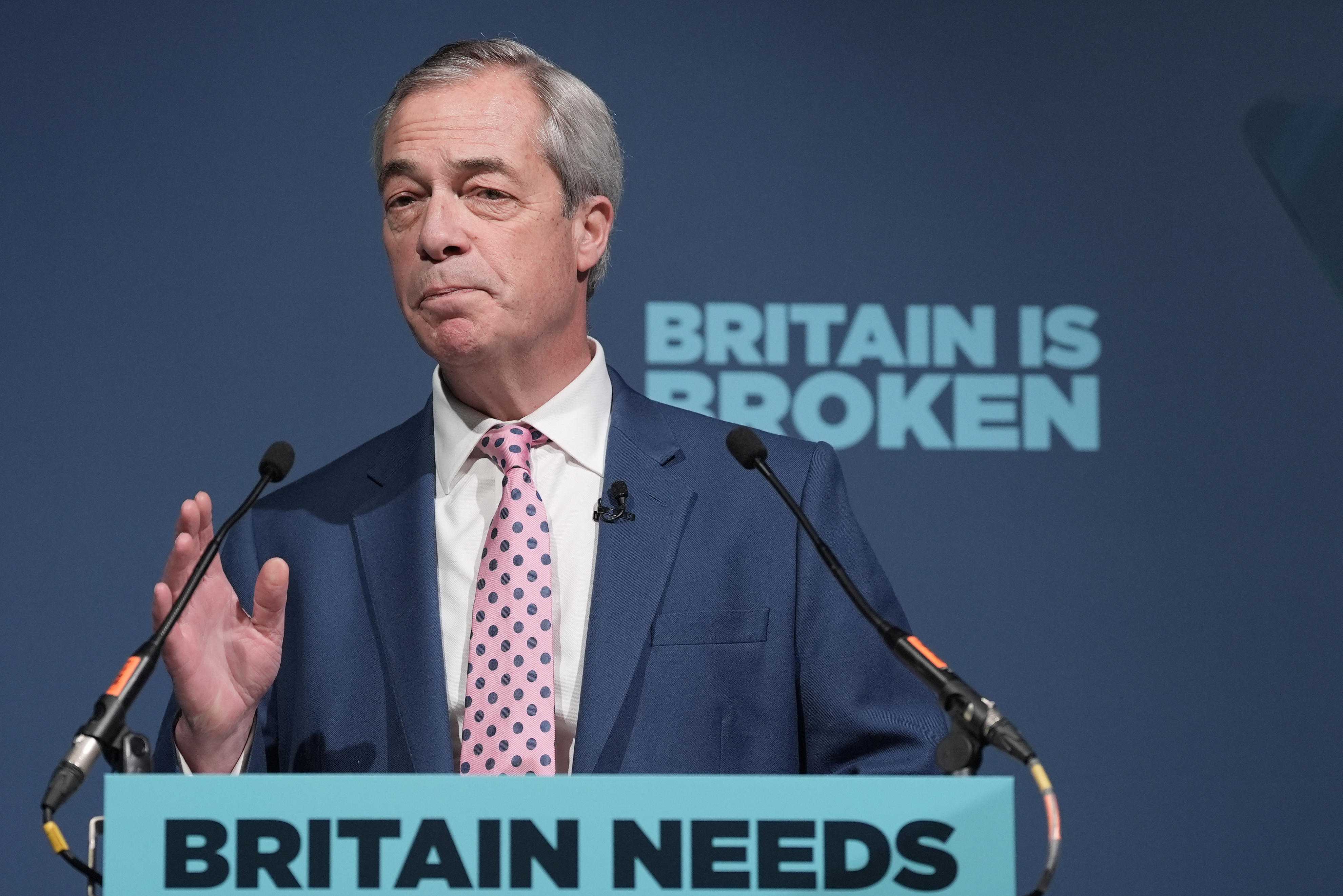 Nigel Farage at a lectern with Reform UK backdrop and the words Britain Is Broken