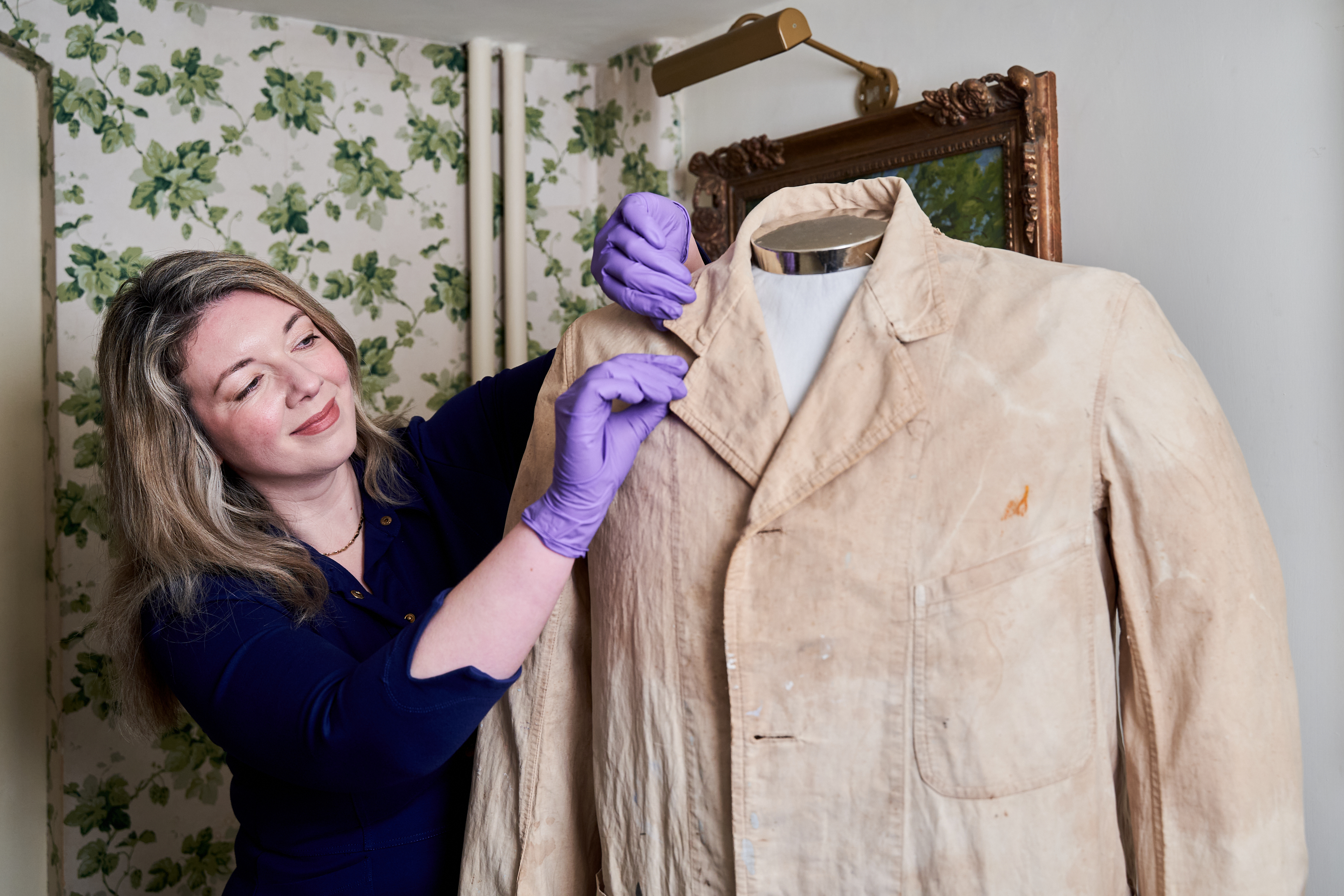 Curator Katherine Carter smiling while adjusting the collar of a white coat on display