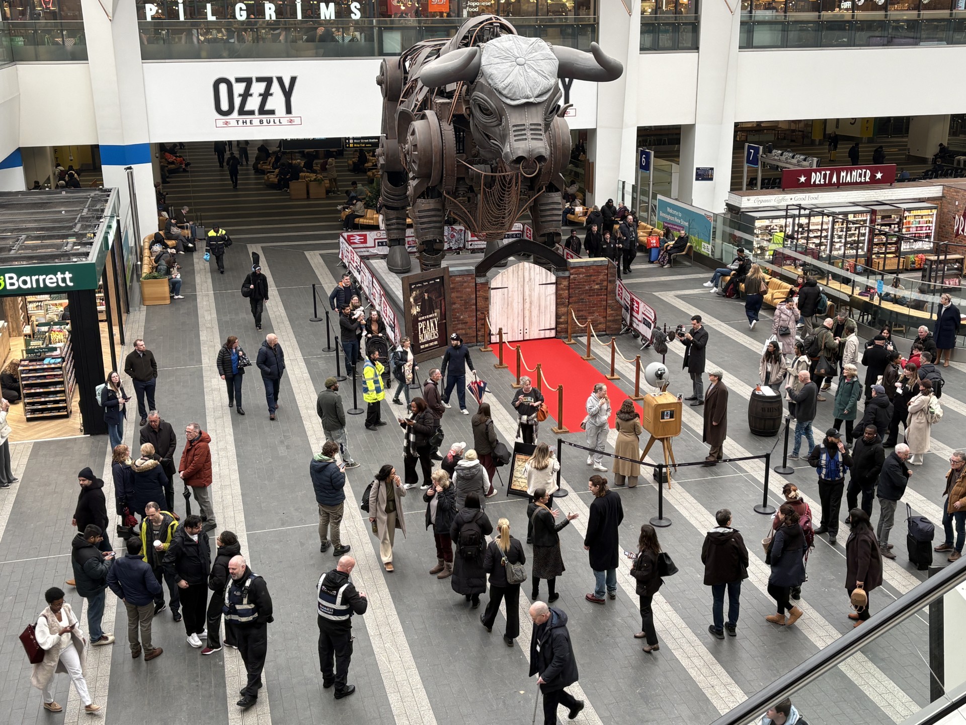A view of Birmingham New Street station concourse, with Ozzy the Bull wearing a flat cap and a red carpet leading up to it