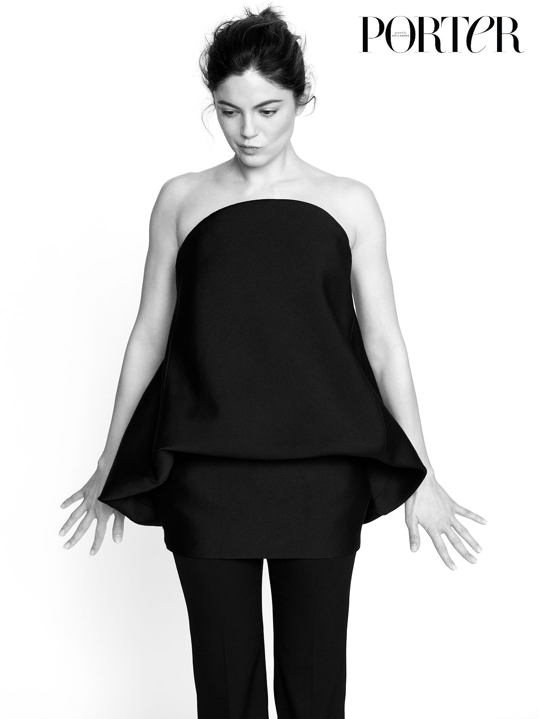 A black and white photo of Monica Barbaro posing in black tunic and trousers, with Porter in the top corner of the image