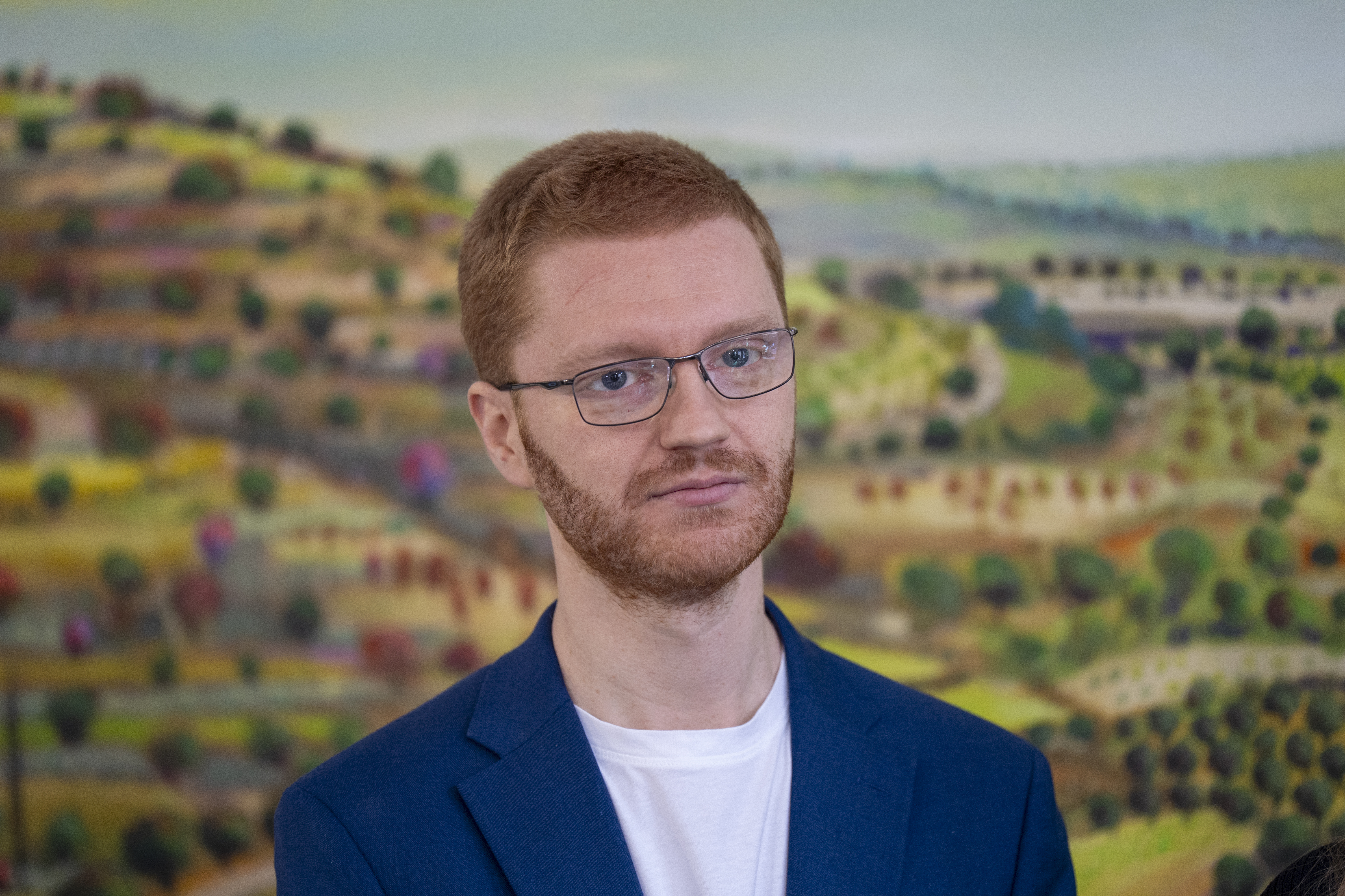Head and shoulders photo of Ross Greer, wearing a white T-shirt and blazer