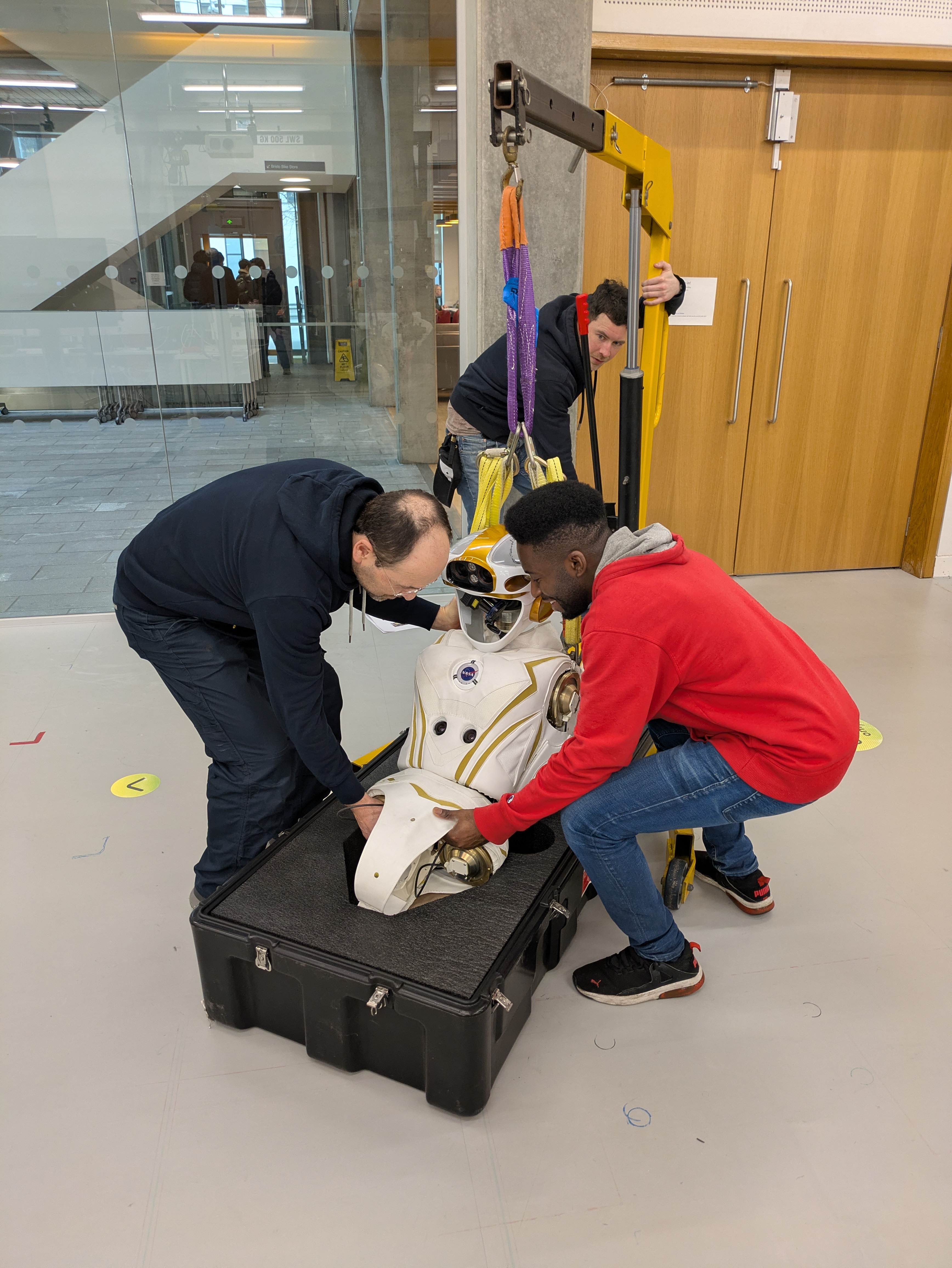 Three men work to place part of a robot into a protective case
