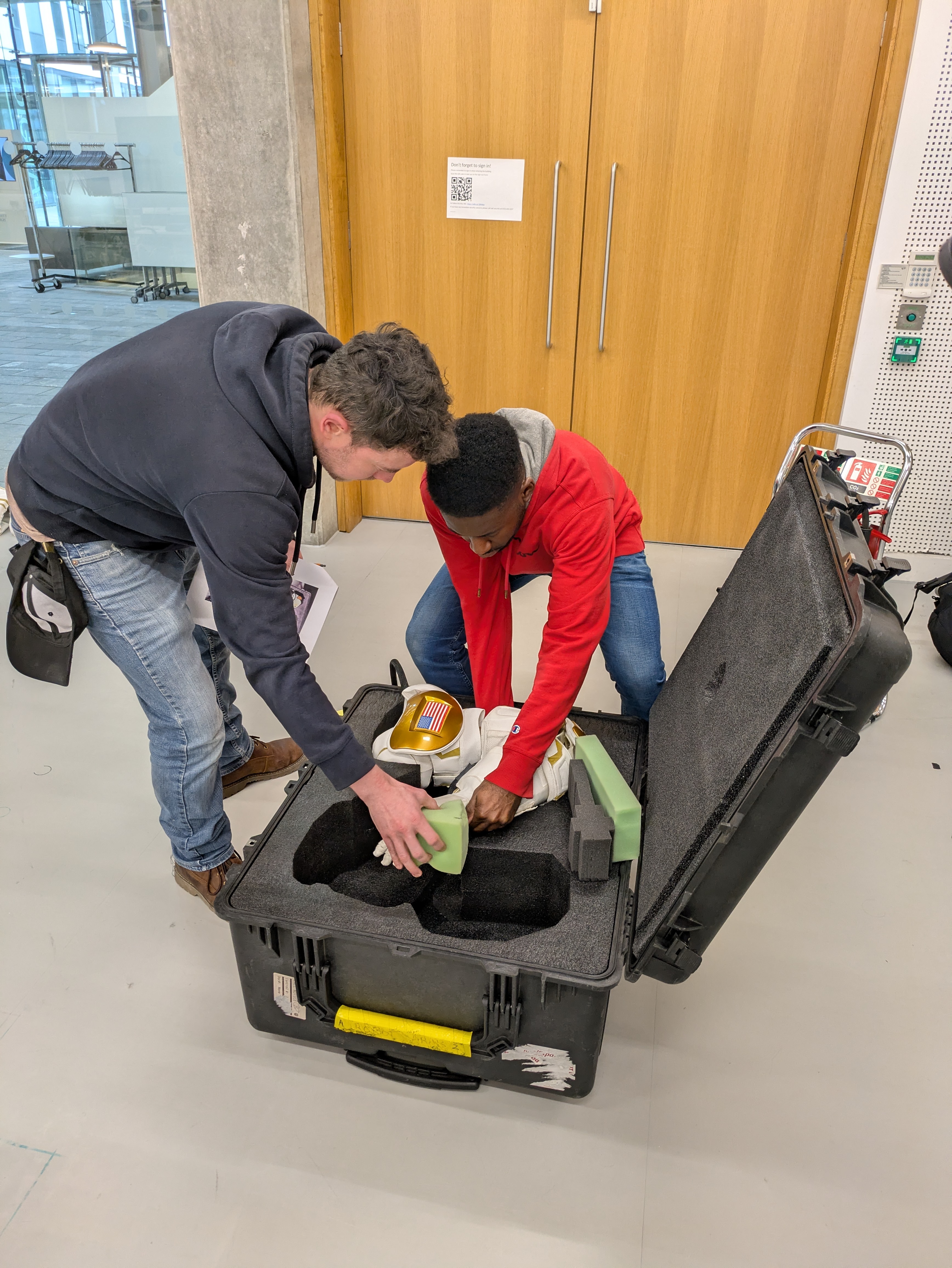 Two men place parts of a robot into a protective case