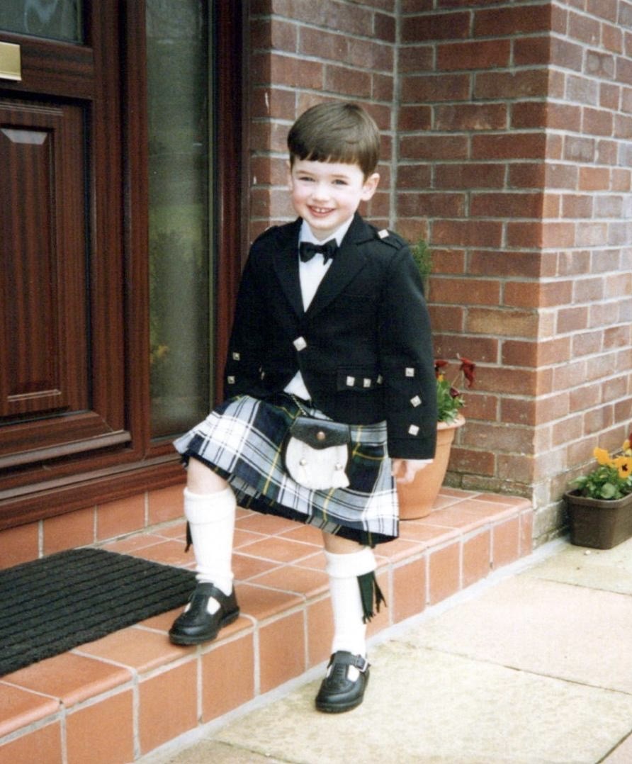 Ross Irvine smiling while posing on a doorstep and wearing a kilt