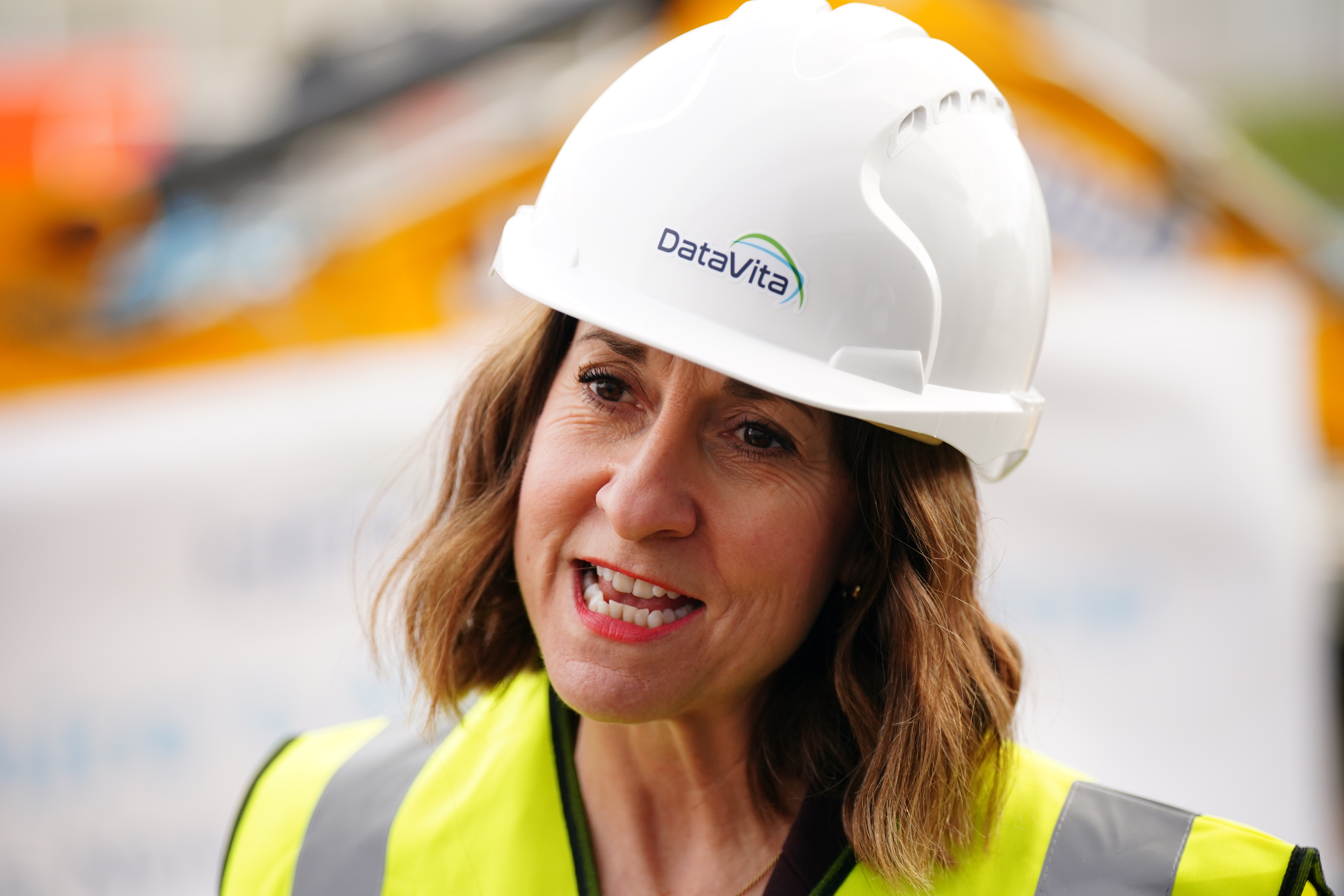 Liz Kendall speaking, while wearing a white hard hat and a yellow hi-vis best