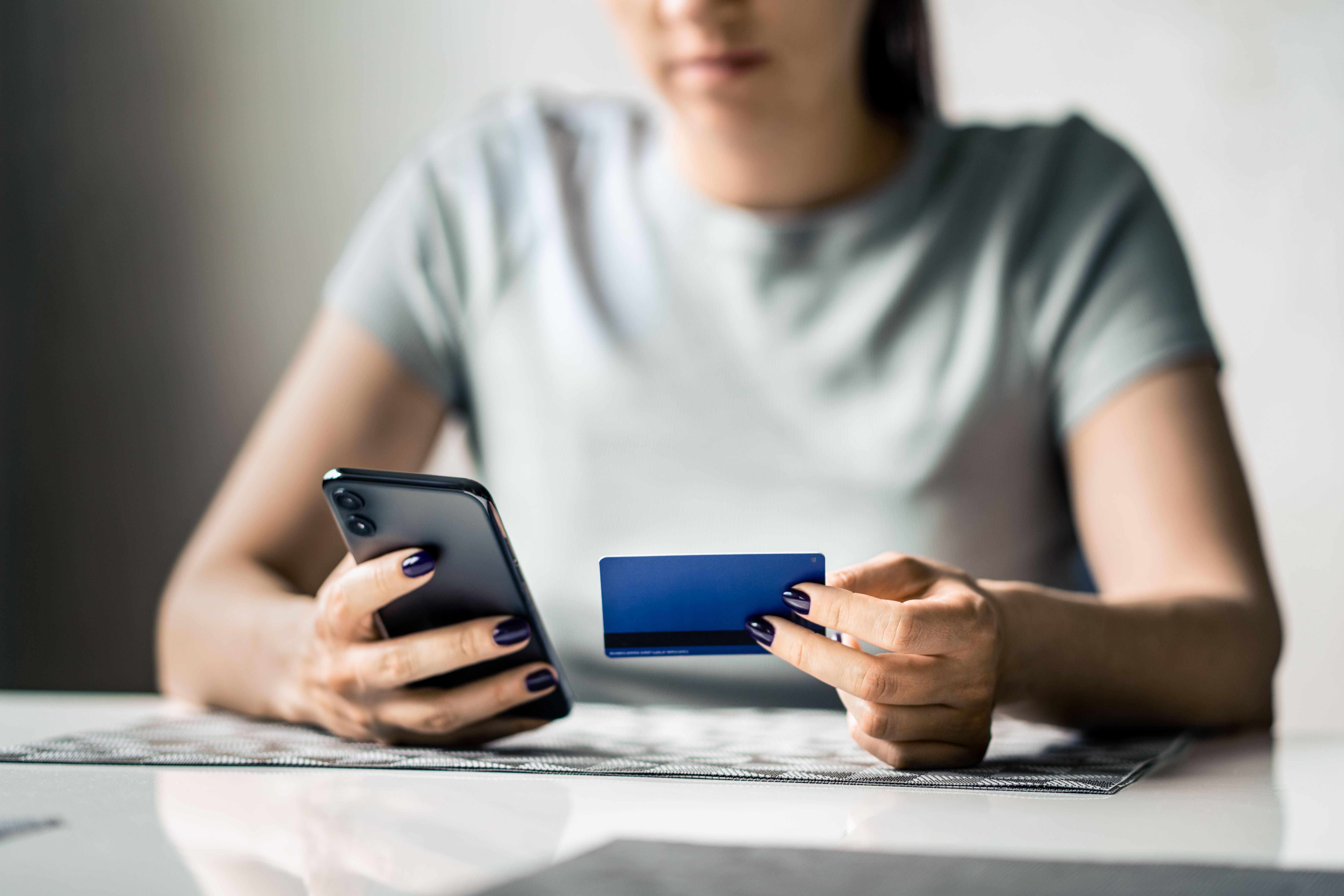A person looking at her phone and holding a bank card