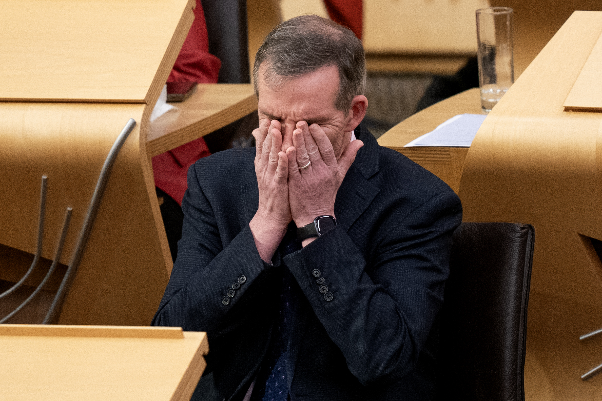 Liam McArthur seated in Parliament, with his hands over his face