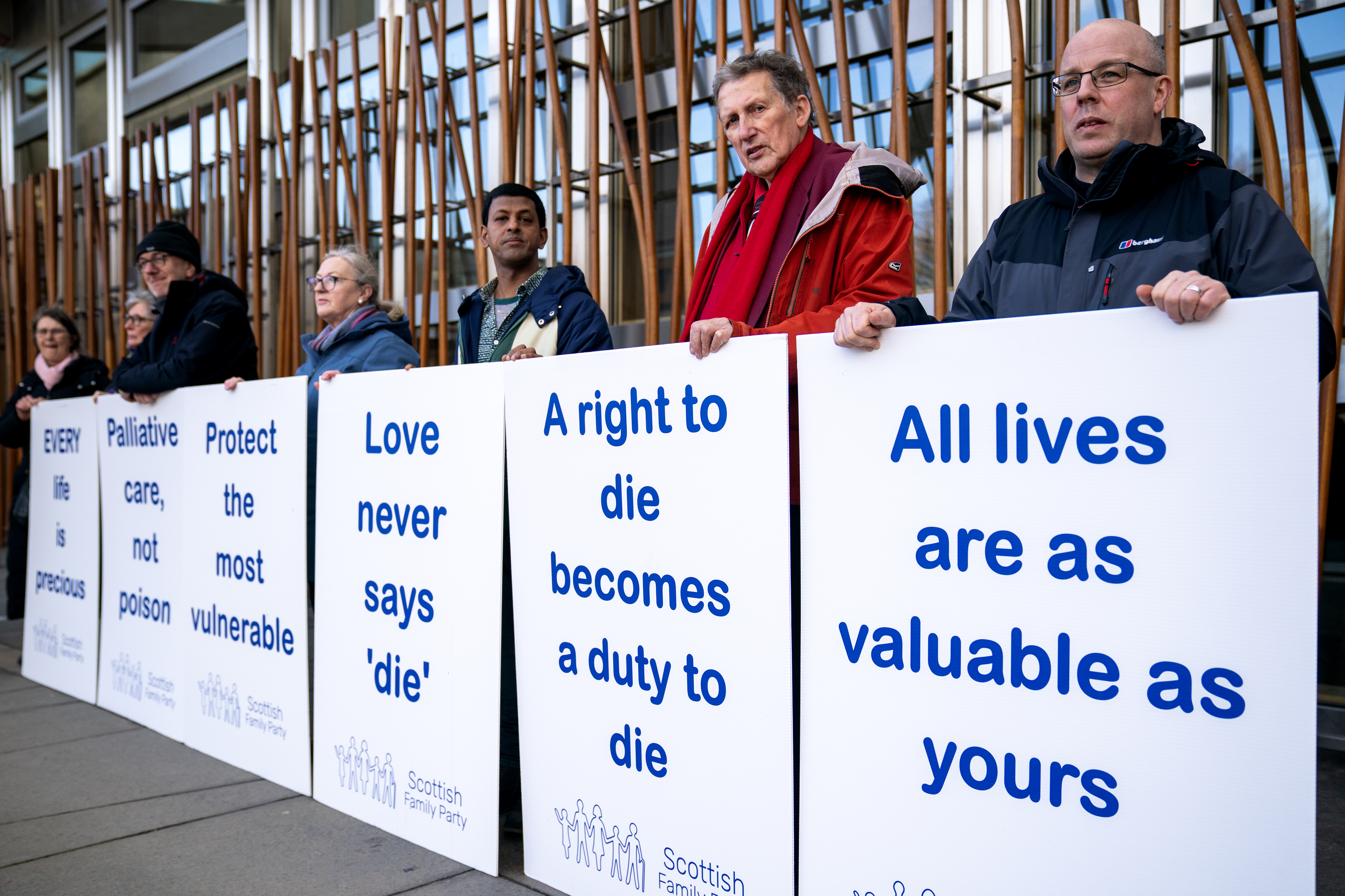 Opponents of assisted dying standing outside Holyrood with posters which read 'A right to die becomes a duty to die', and 'All lives are as valuable as yours'