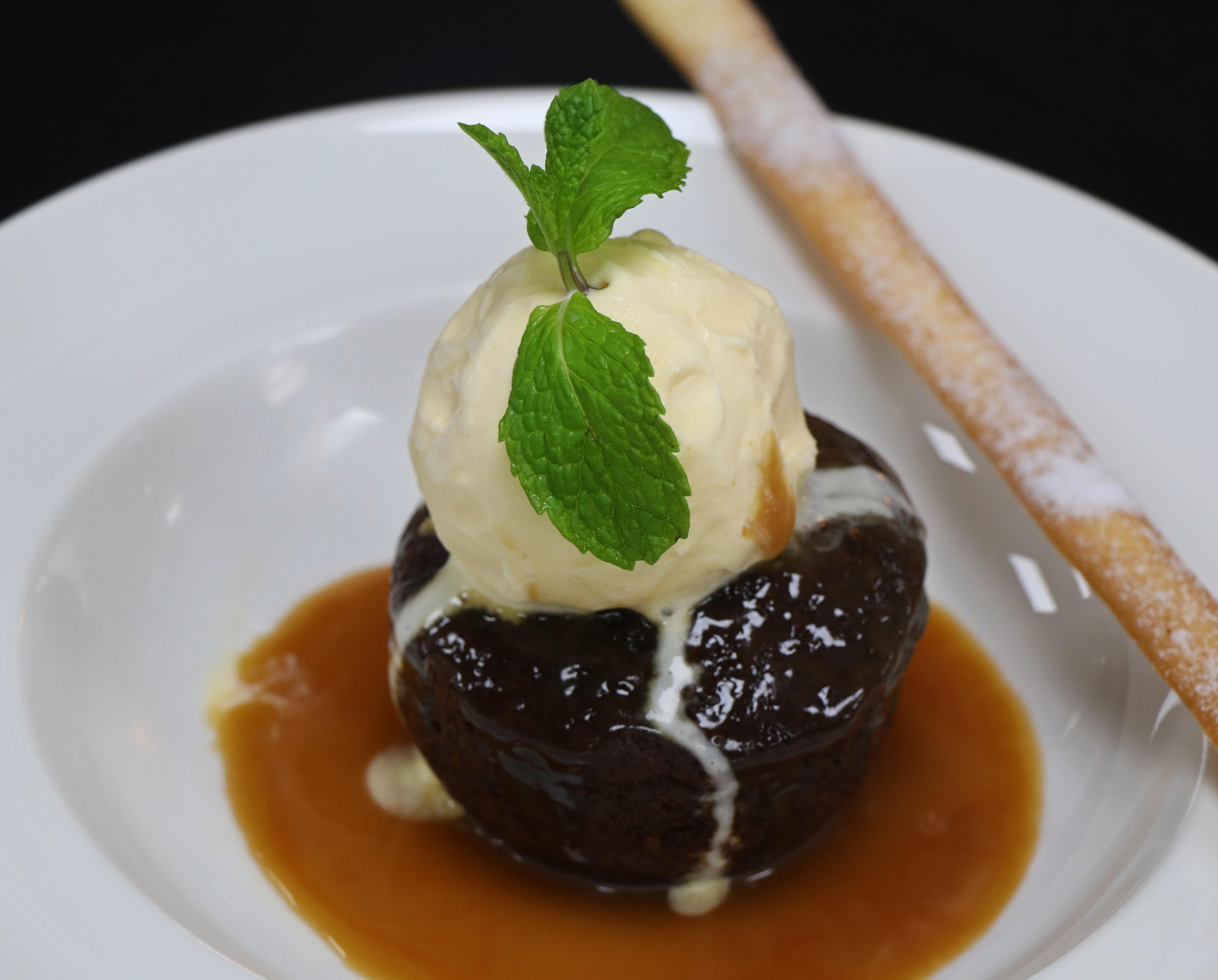 Sticky toffee pudding with vanilla ice cream and caramel sauce and mint garnish