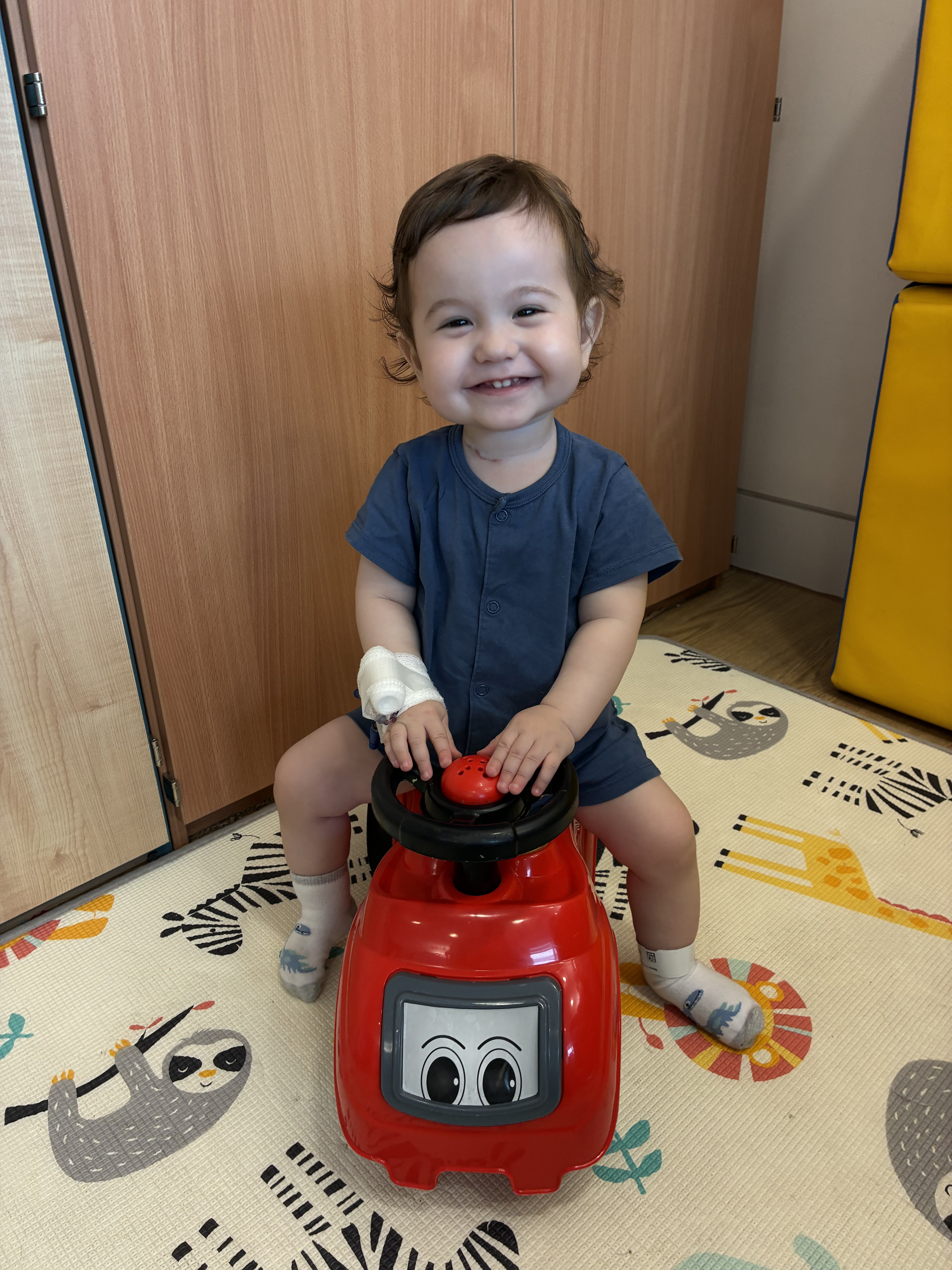 Casey McIntyre sitting on a toy car and smiling
