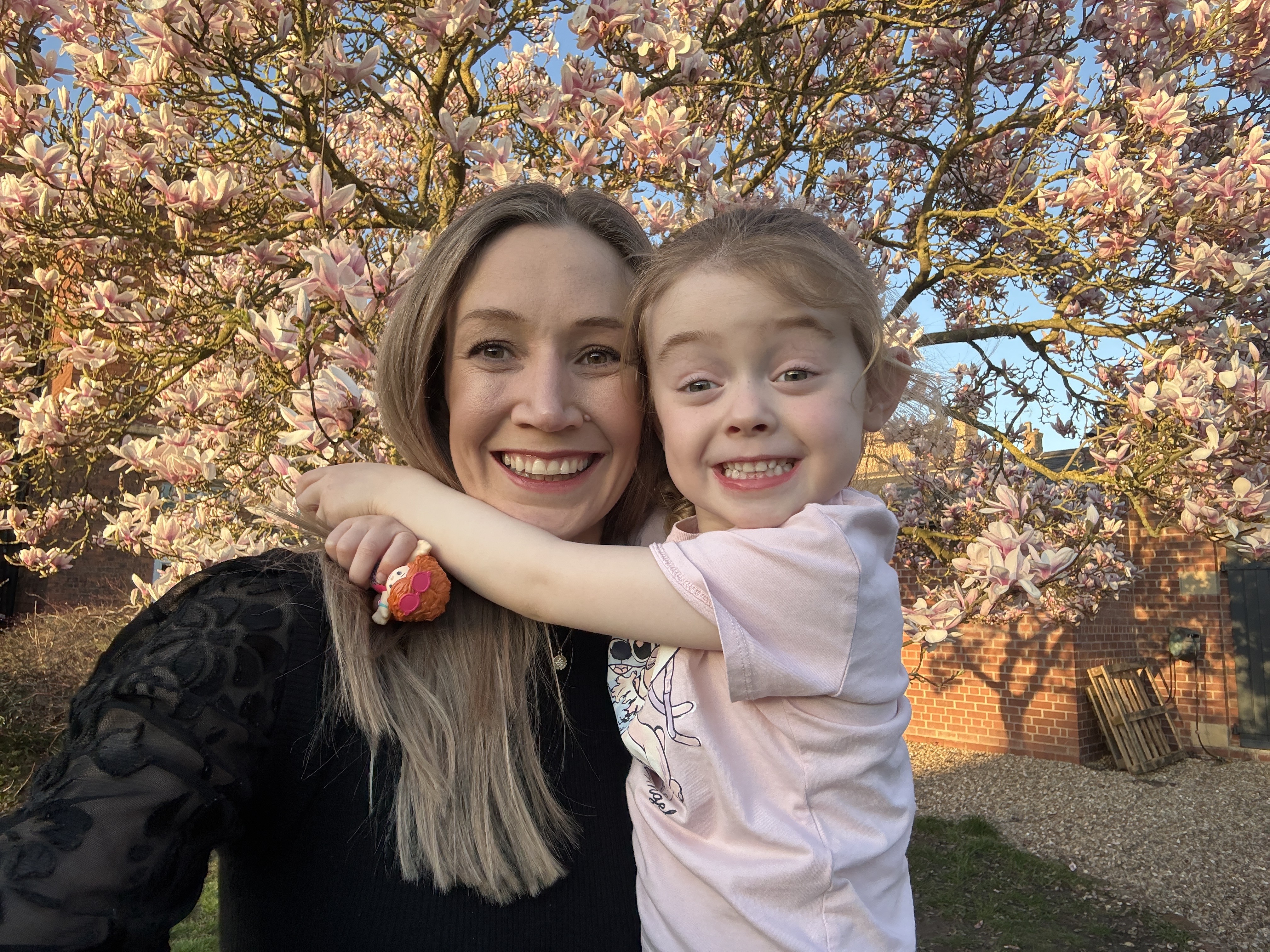 Laura Cororan smiling while cuddling with a young girl in front of a tree in blossom