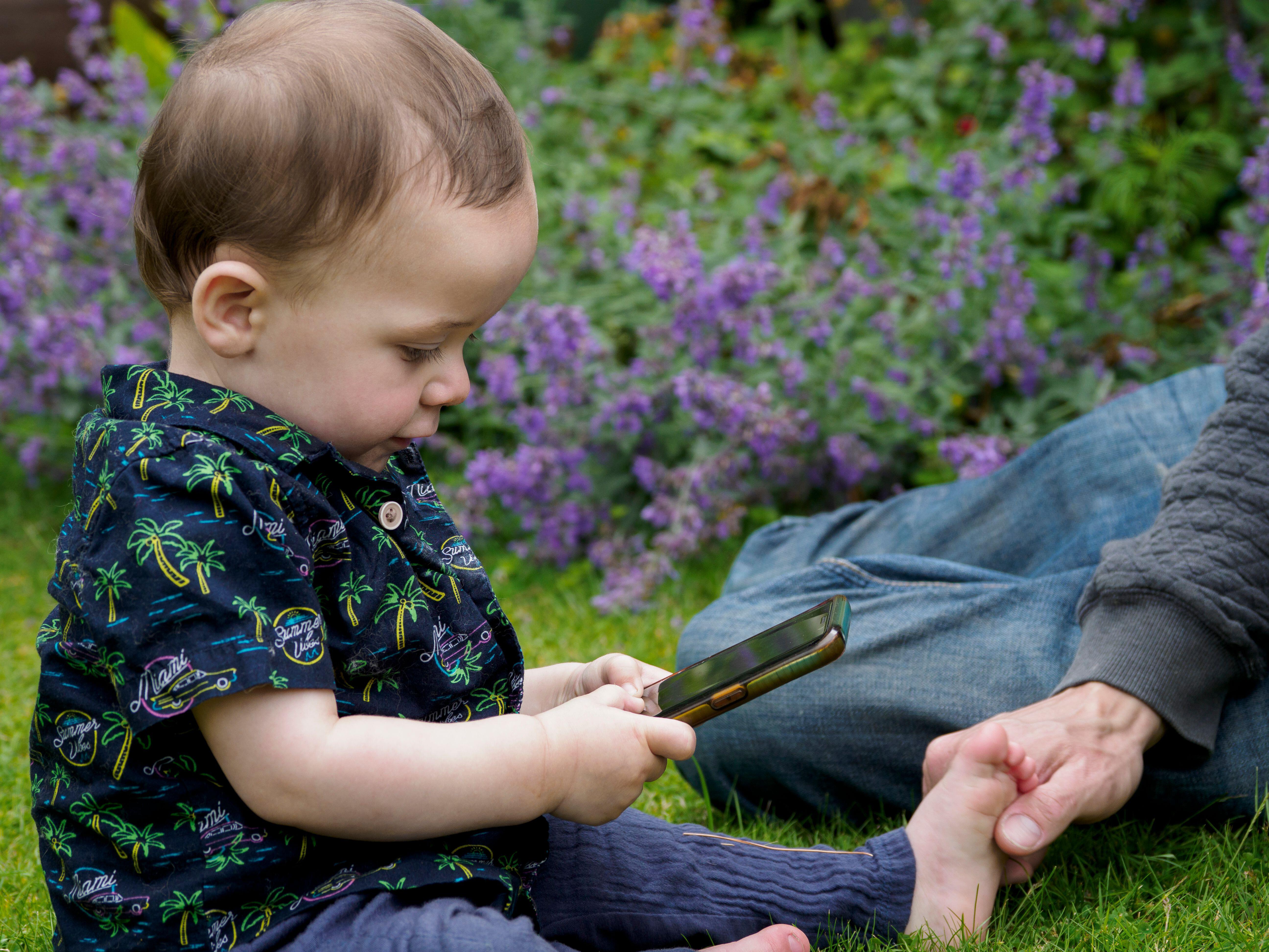 A toddler sitting on grass playing with a mobile phone